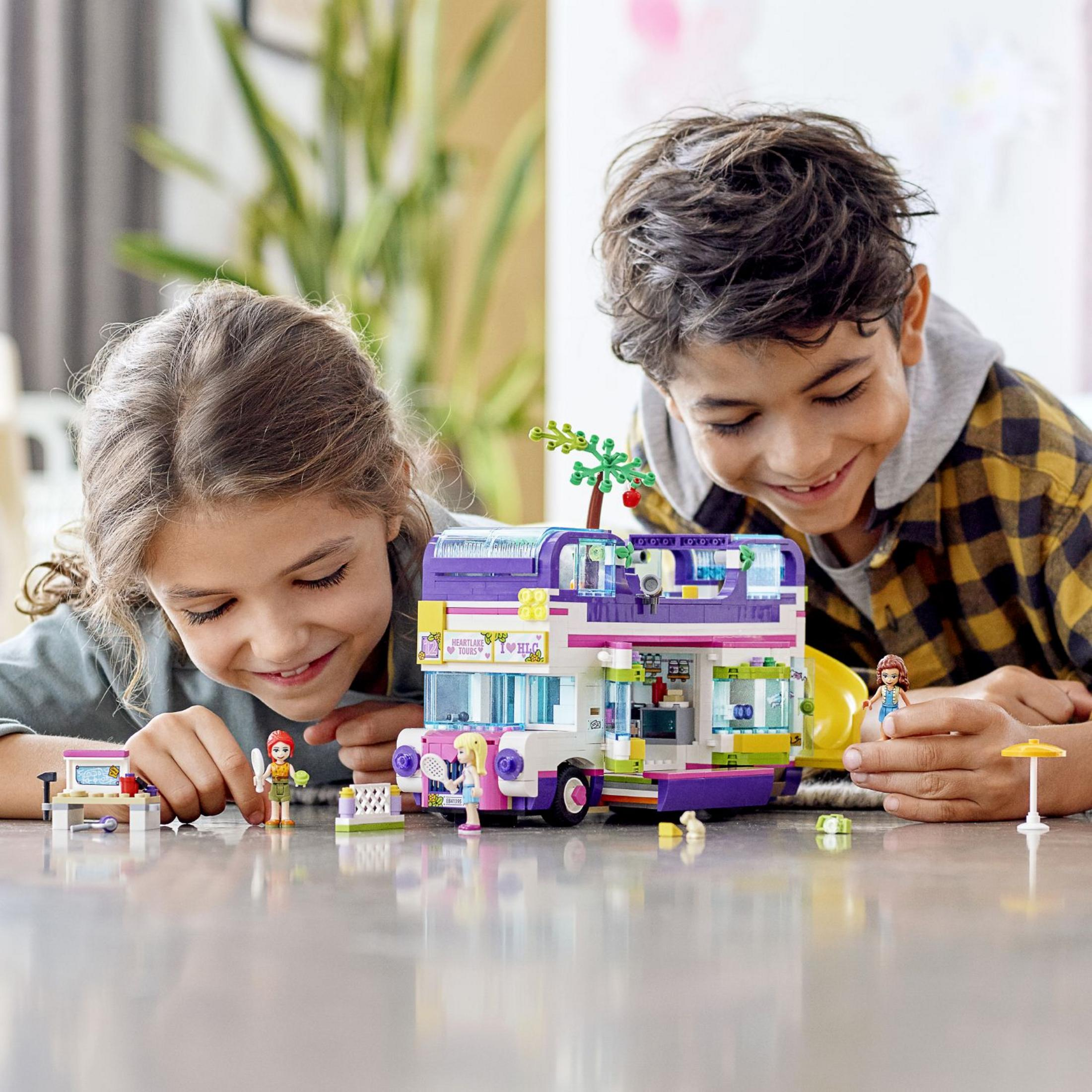 Zwei Kinder spielen mit einem Lego-Bus und lächeln das Spielzeug an.