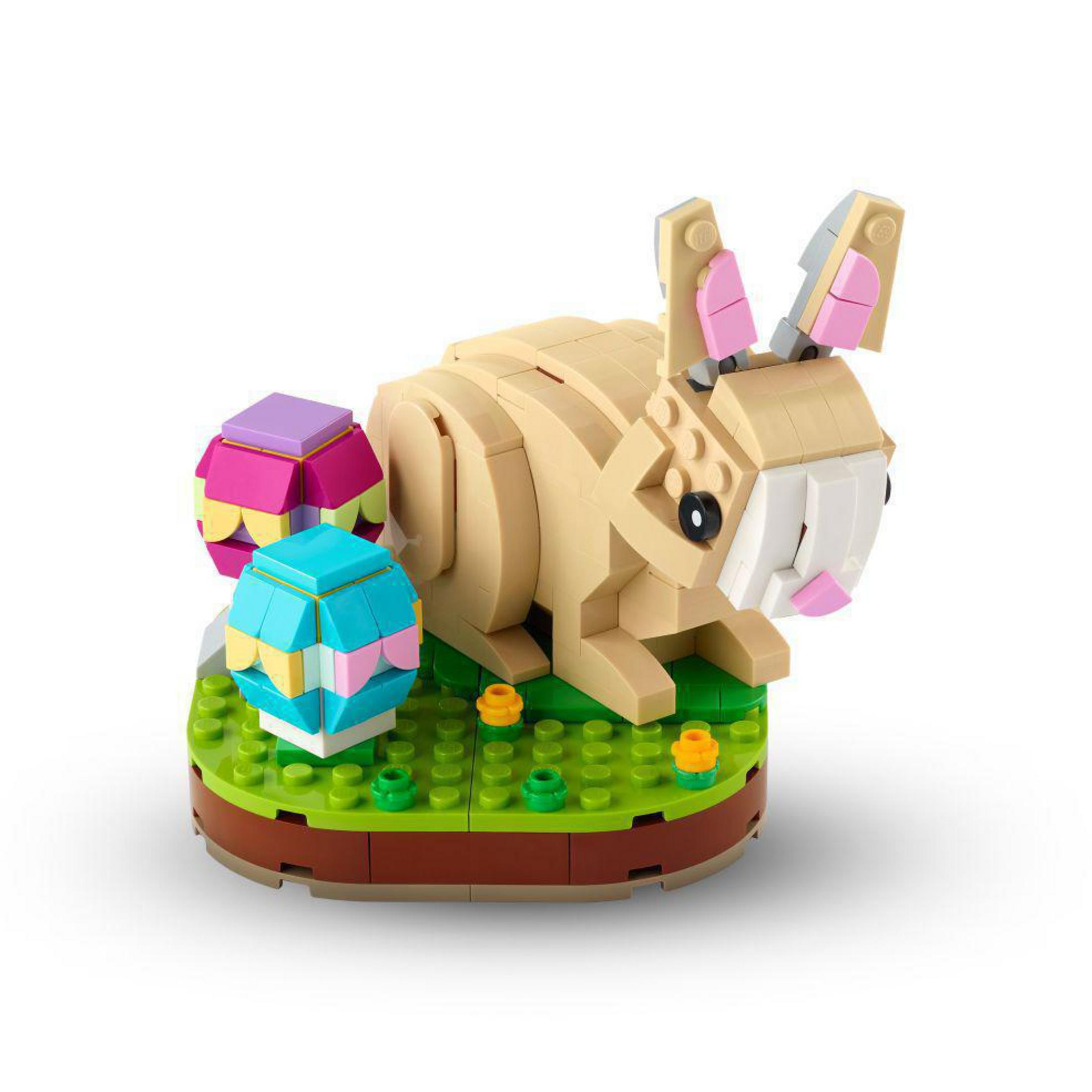 Zajączek wielkanocny LEGO z dwoma zdobionymi jajkami na zielonej podstawie z kwiatami.