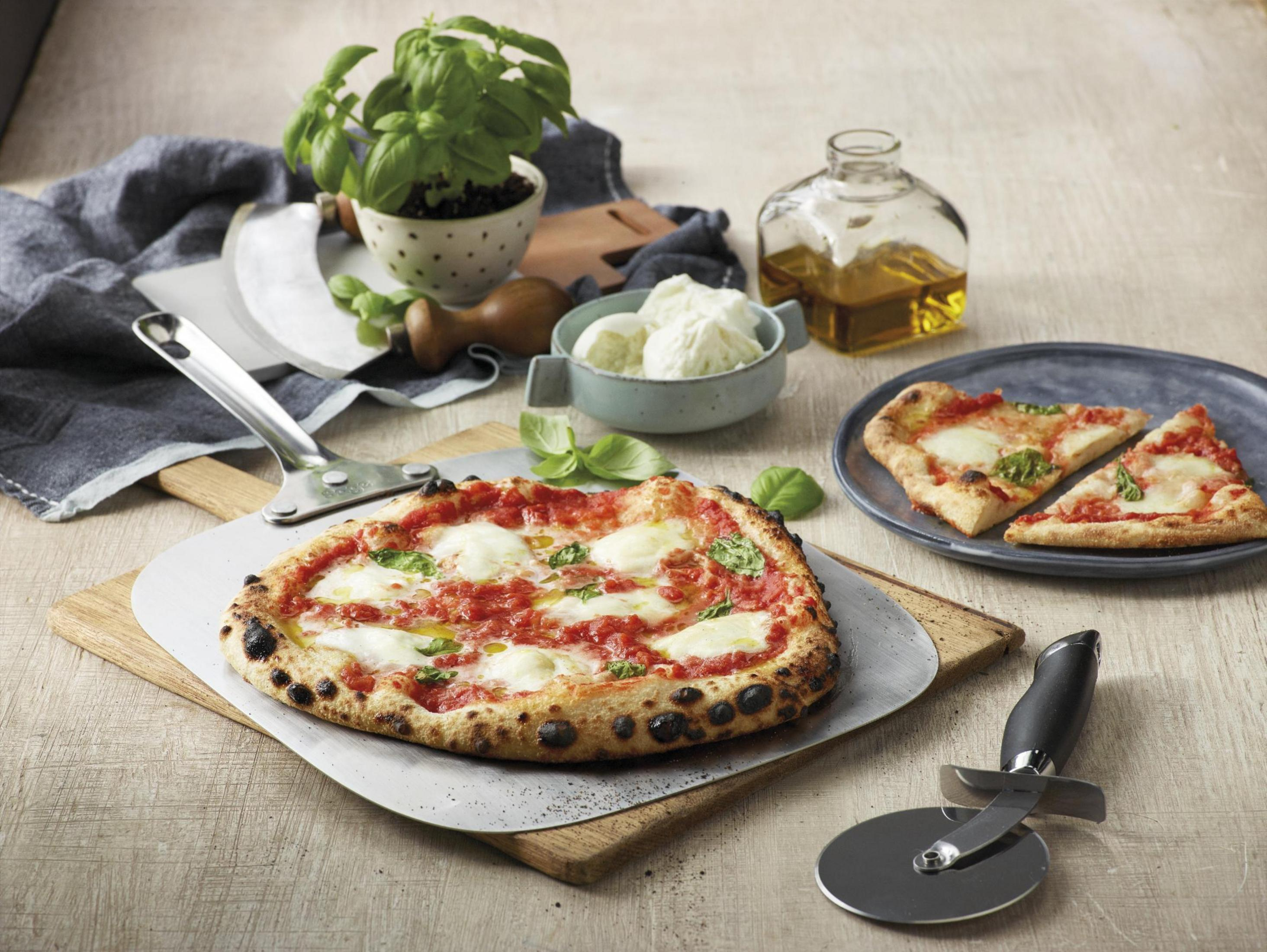 Una pizza su una tavola di legno con basilico e ingredienti, pronta per essere mangiata.