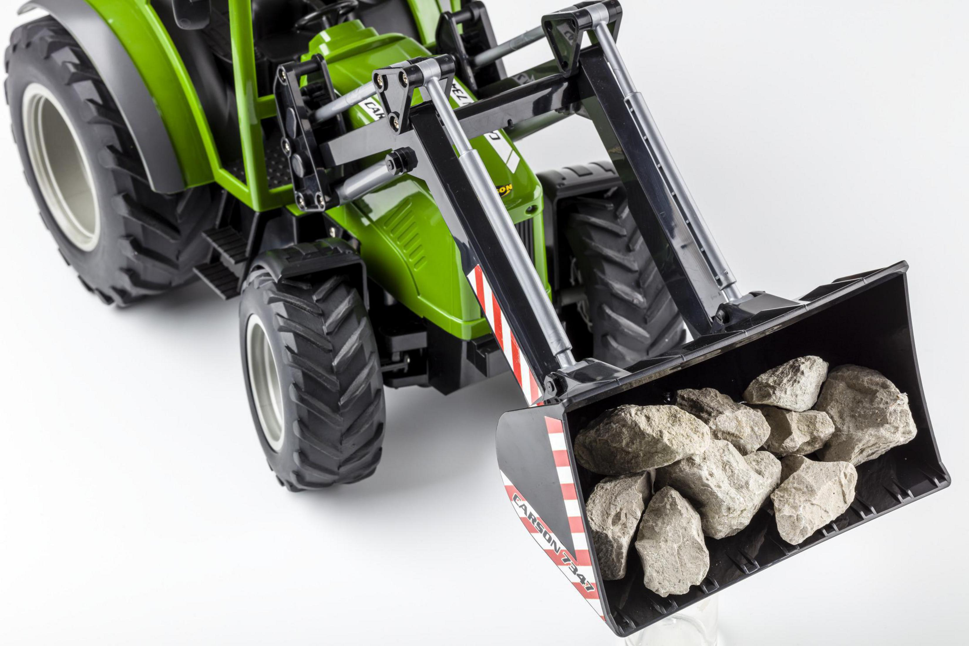 Grüner Spielzeugtraktor mit Frontlader, der Steine transportiert, vor weißem Hintergrund.