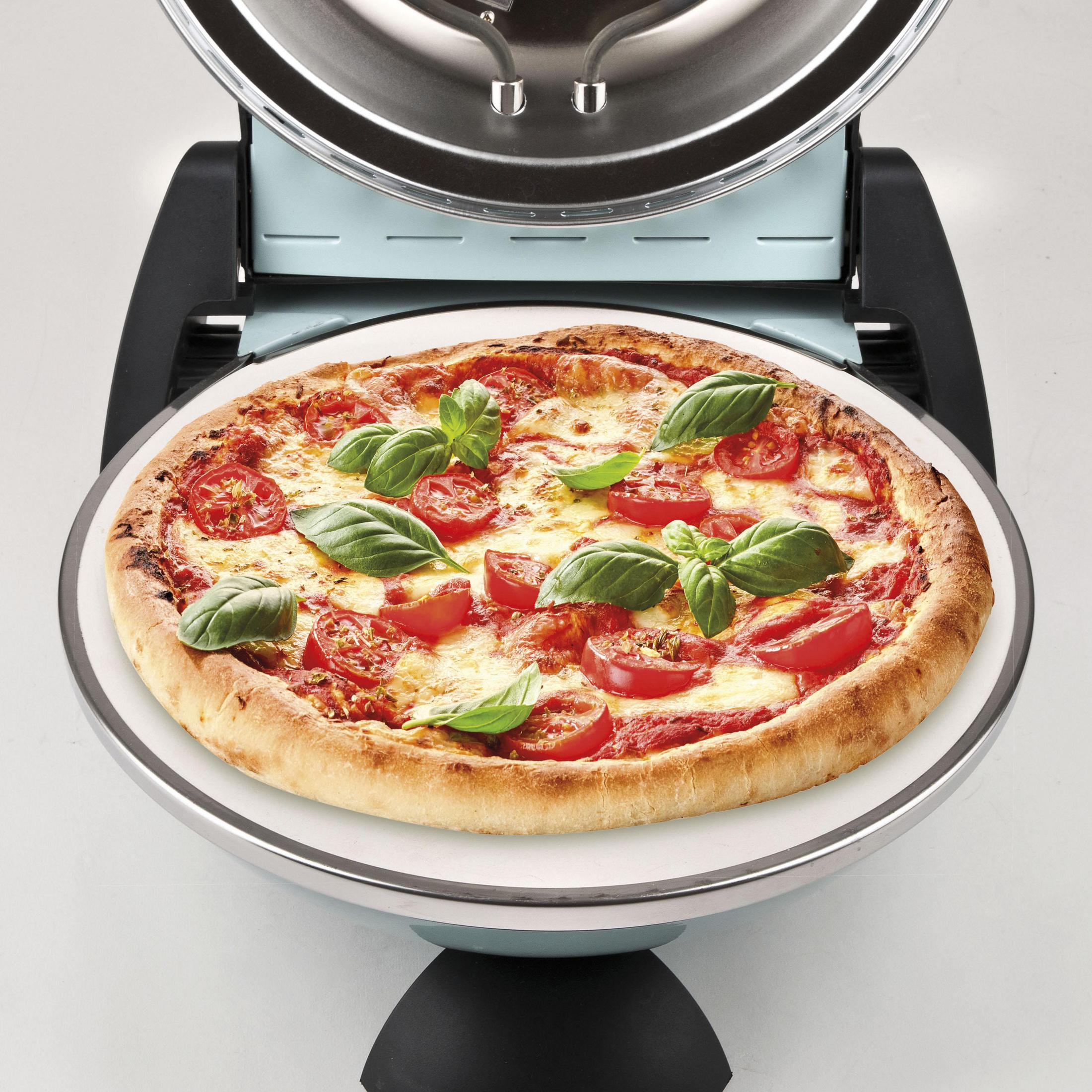 Pizza su un piatto bianco, con pomodori, basilico e formaggio fuso. Forno aperto.