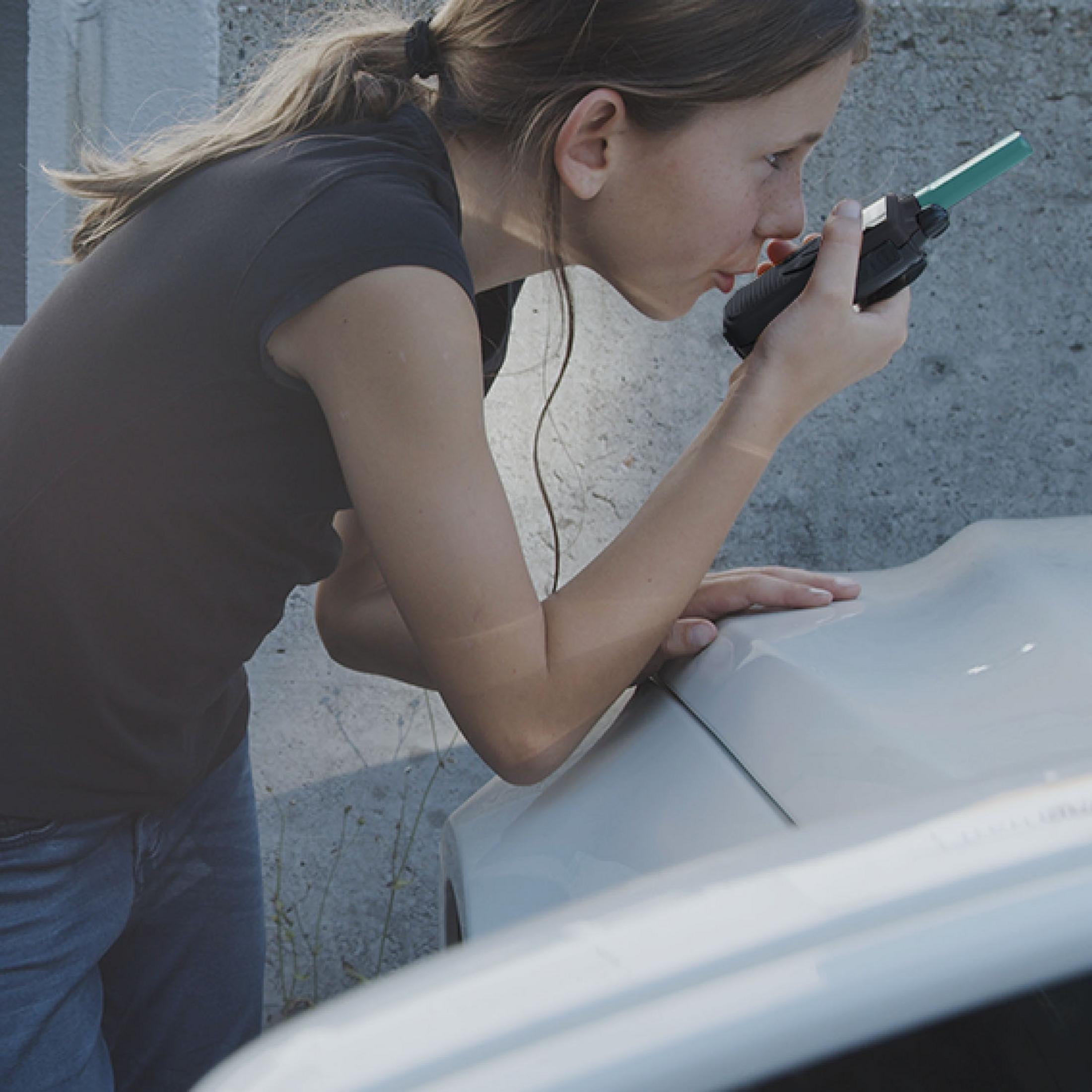 Eine Frau lehnt sich über ein Auto und hält ein Funkgerät an den Mund.