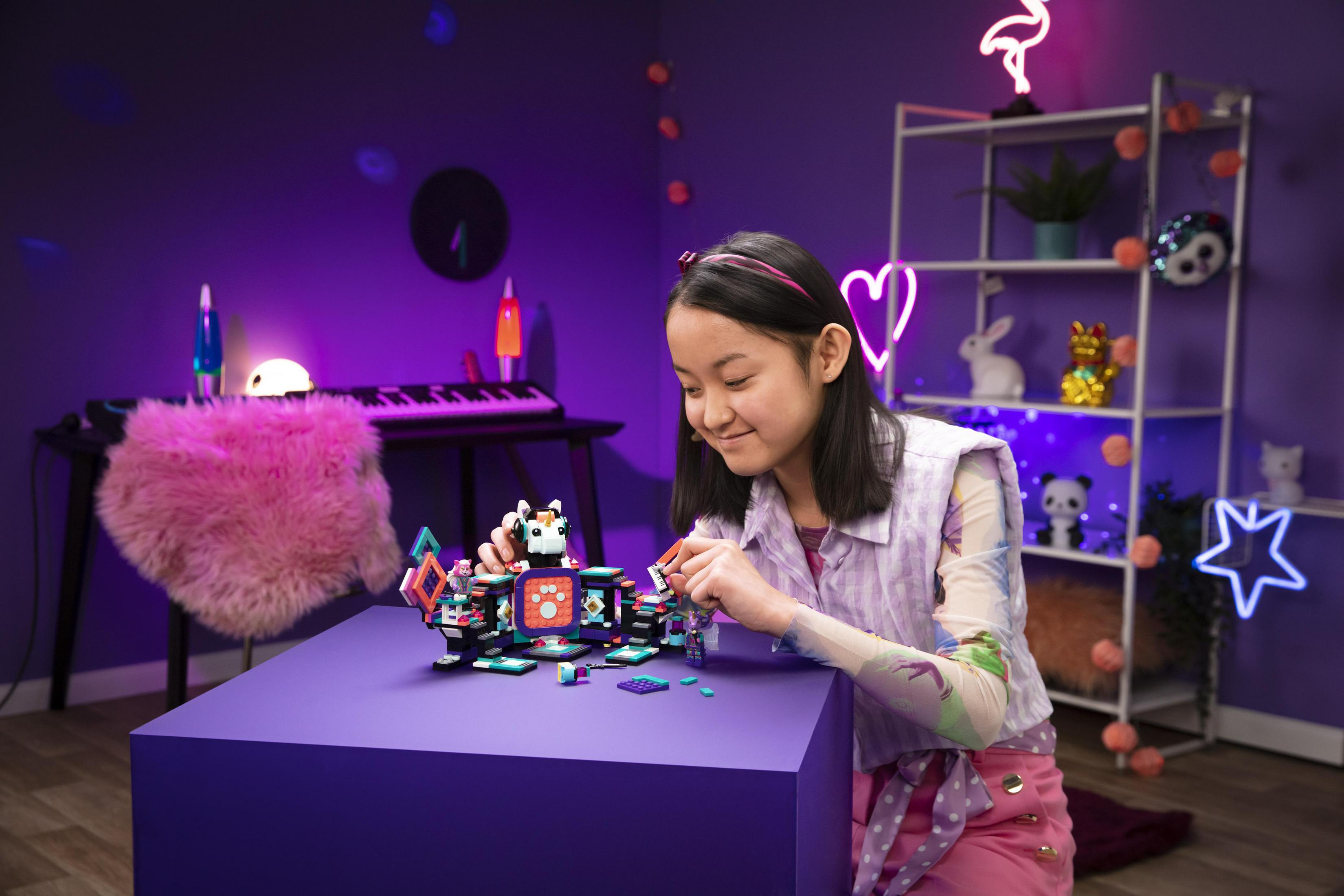 Dziewczyna budująca zestaw Lego na fioletowym stole w fioletowym pokoju z neonowymi dekoracjami.