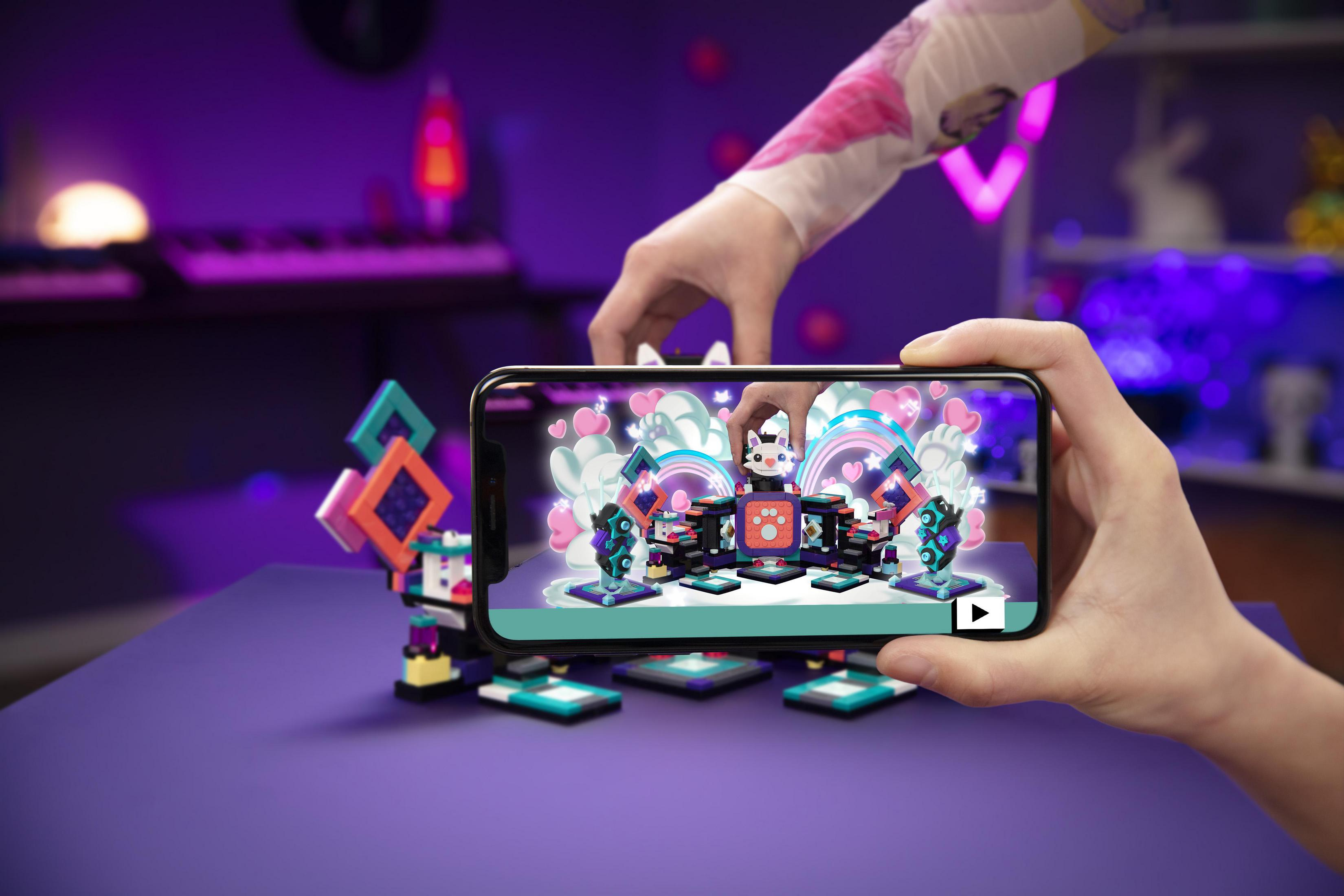 Osoba trzymająca telefon pokazujący zestaw Lego z kotem DJ i światłami w kształcie serca.