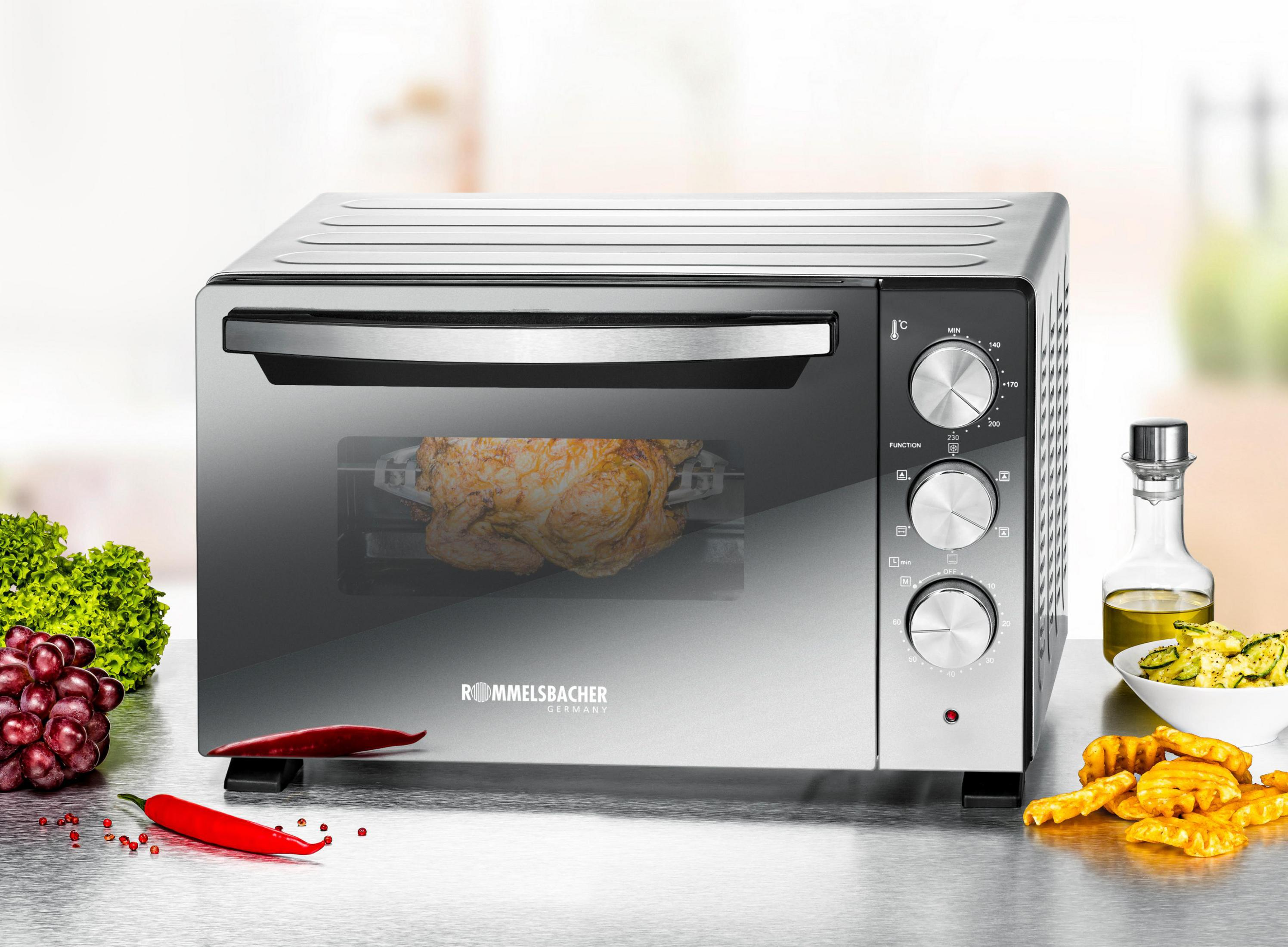 Srebrny piekarnik z pieczonym kurczakiem w środku, z warzywami i butelką oleju.