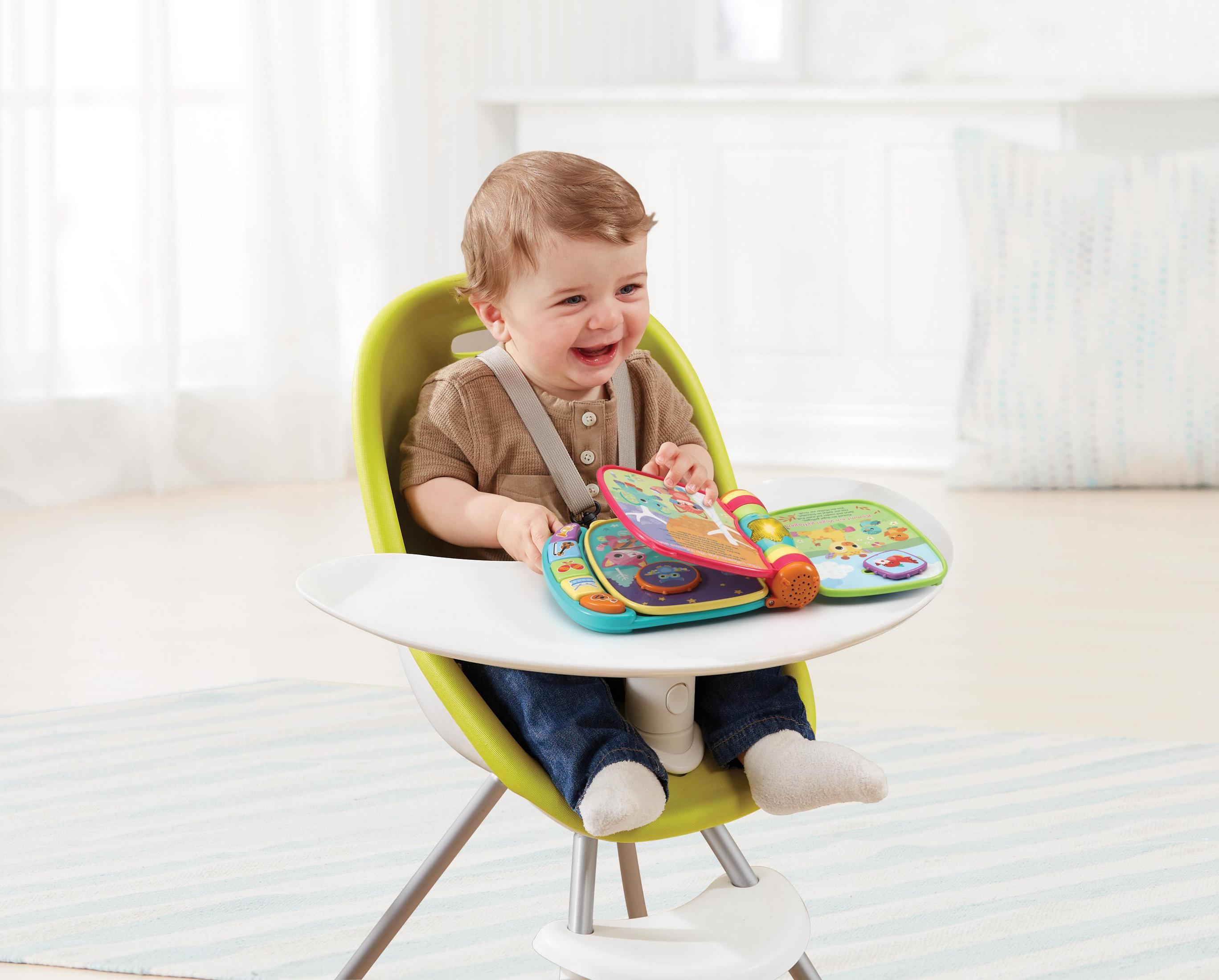 Baby lächelt in einem Hochstuhl und hält ein buntes interaktives Buch.