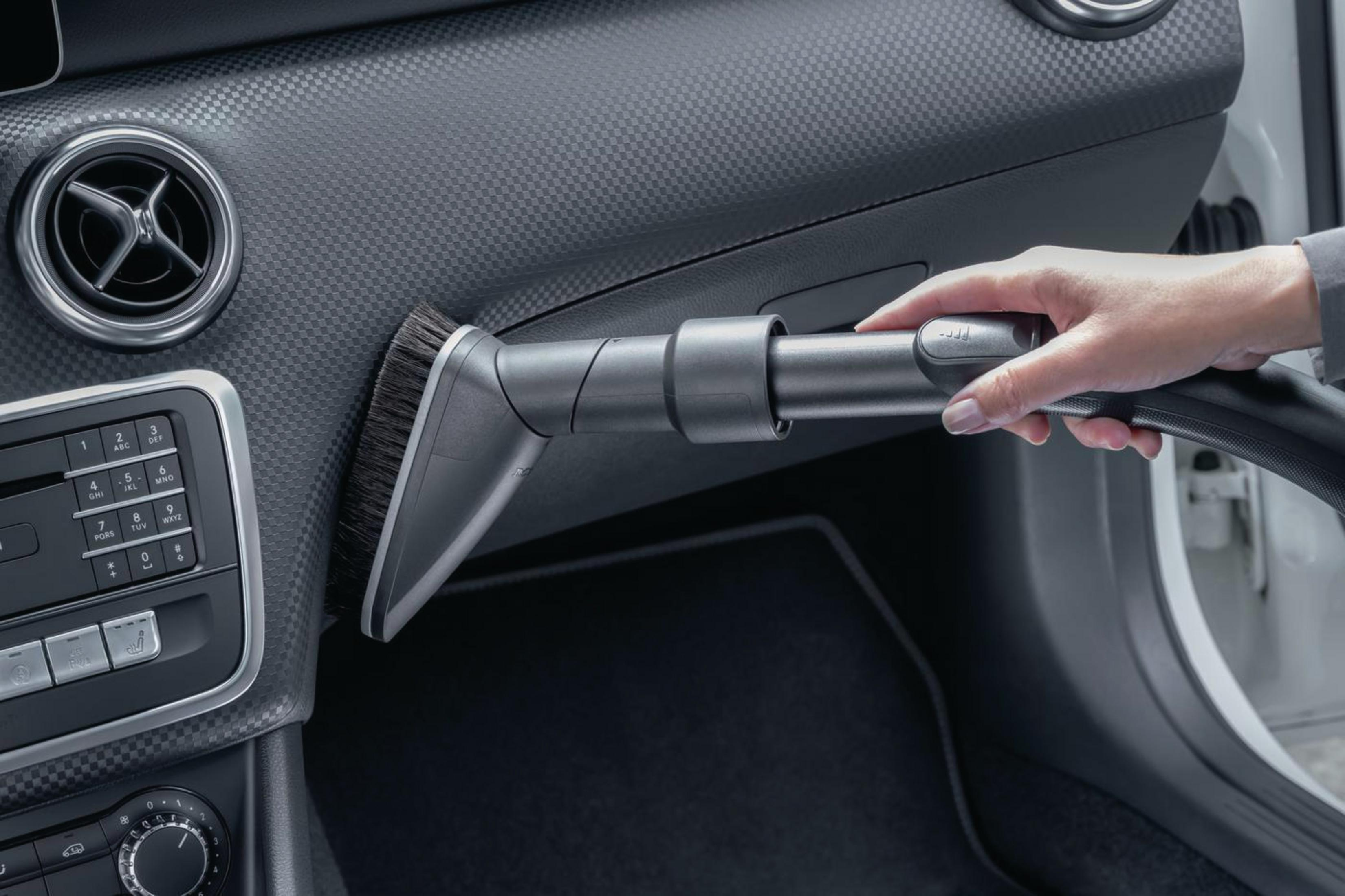 Eine Person, die das Innere eines Autos mit einem Bürstenaufsatz saugt.