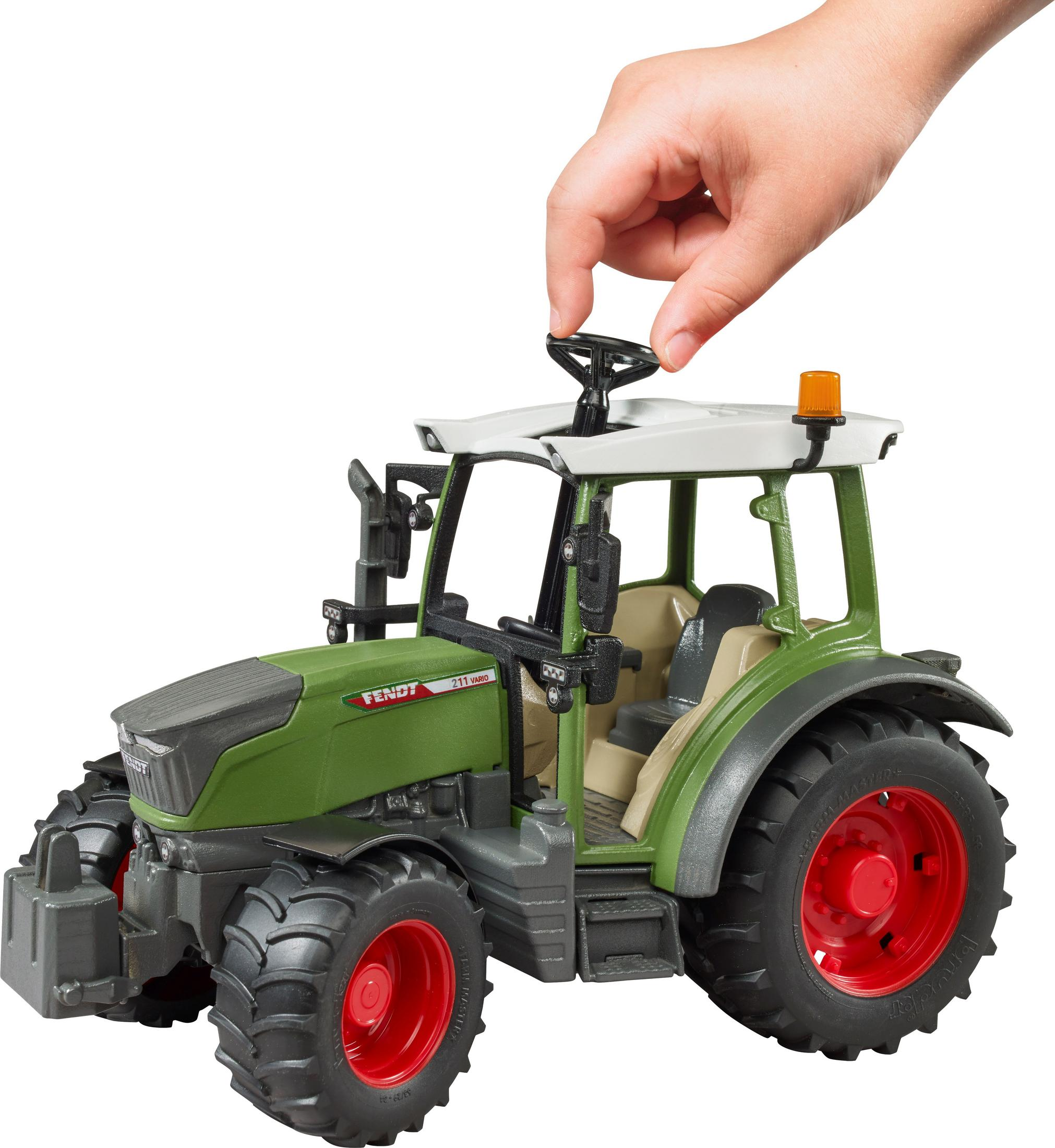 Die Hand eines Kindes berührt einen grünen Spielzeugtraktor. Der Traktor hat rote Räder und ein weißes Dach.