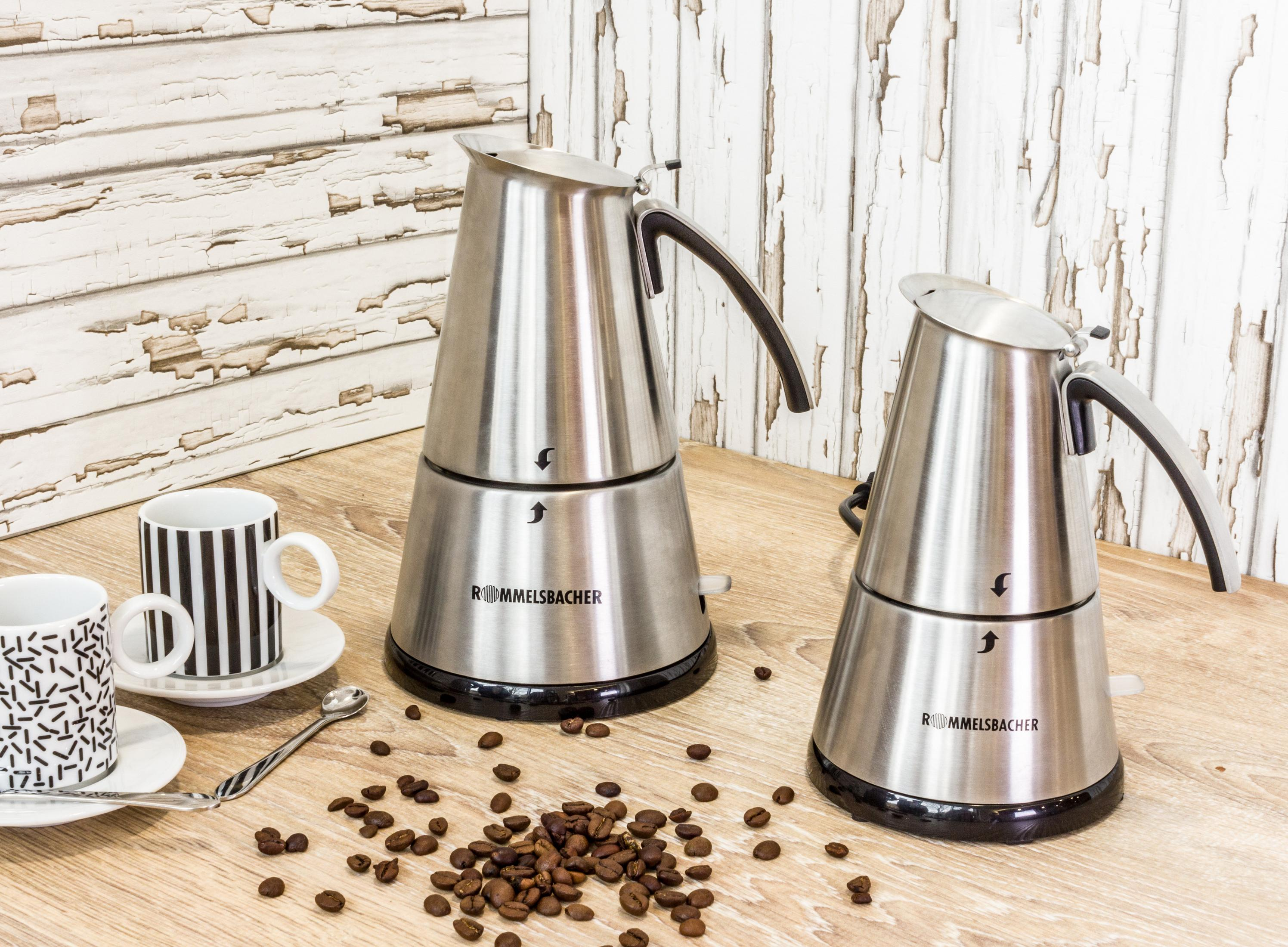 Zwei silberne Kaffeemaschinen auf einem Holztisch. Kaffeebohnen sind verstreut. Zwei Tassen sind daneben.
