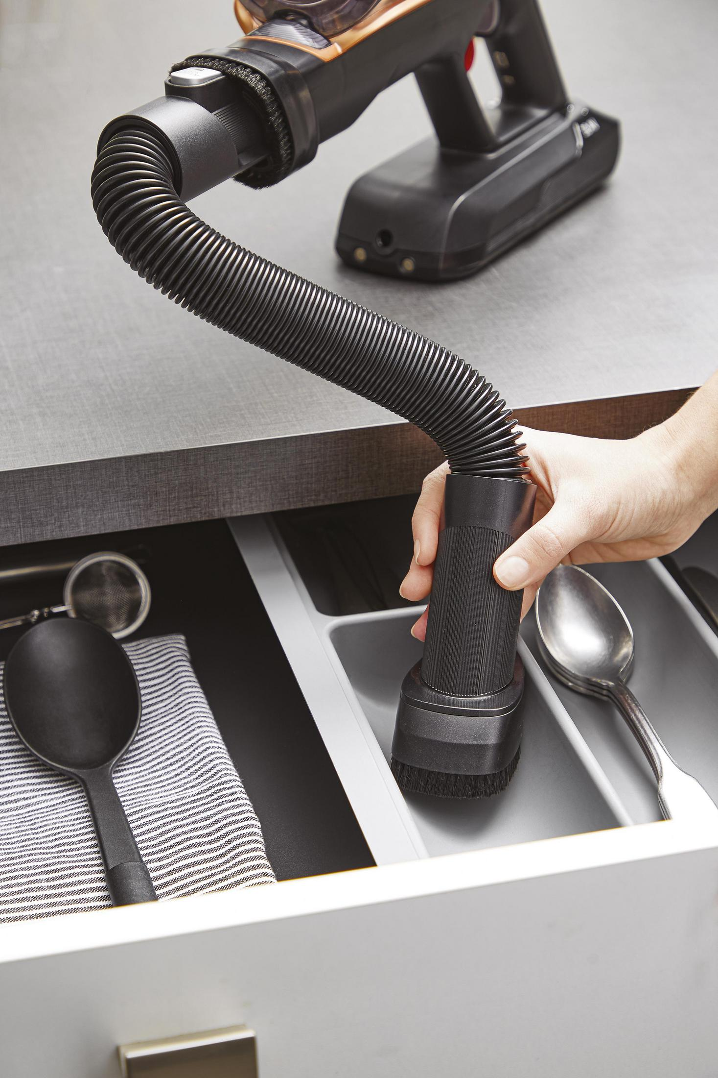 Ręka używająca odkurzacza do czyszczenia szuflady z przyborami.