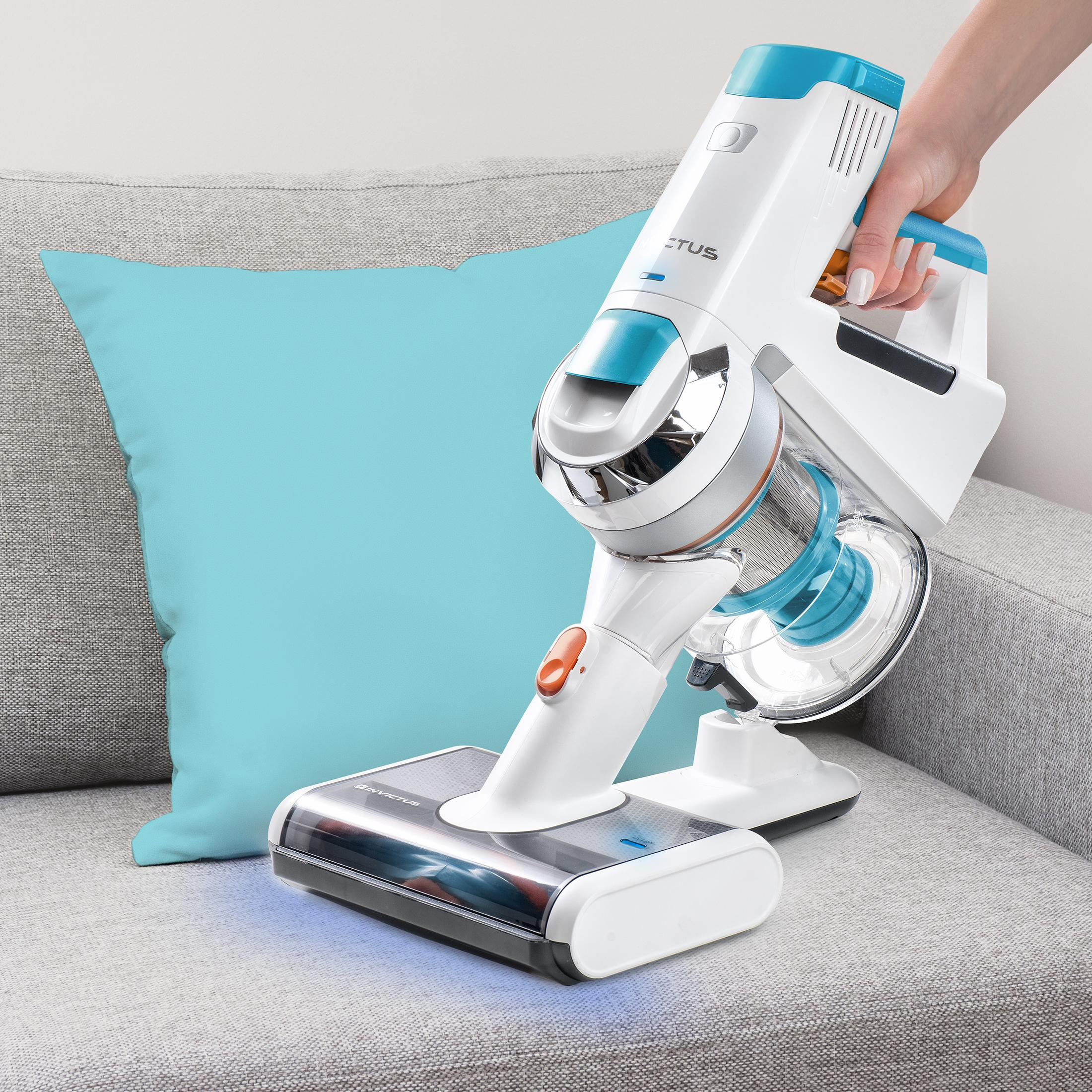 Ein weiß-blauer kabelloser Staubsauger auf einem grauen Sofa. Im Hintergrund ist ein blaues Kissen zu sehen.