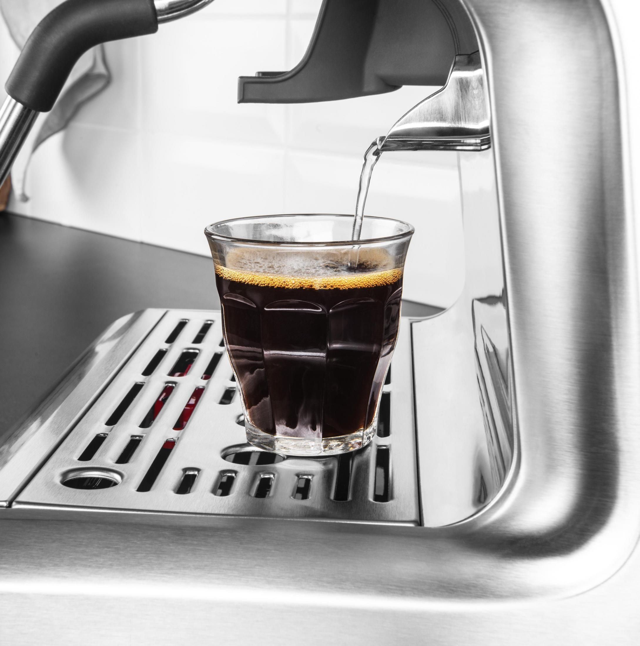 Macchina per espresso che versa caffè in un bicchiere. Acciaio inossidabile, con caffè scuro.