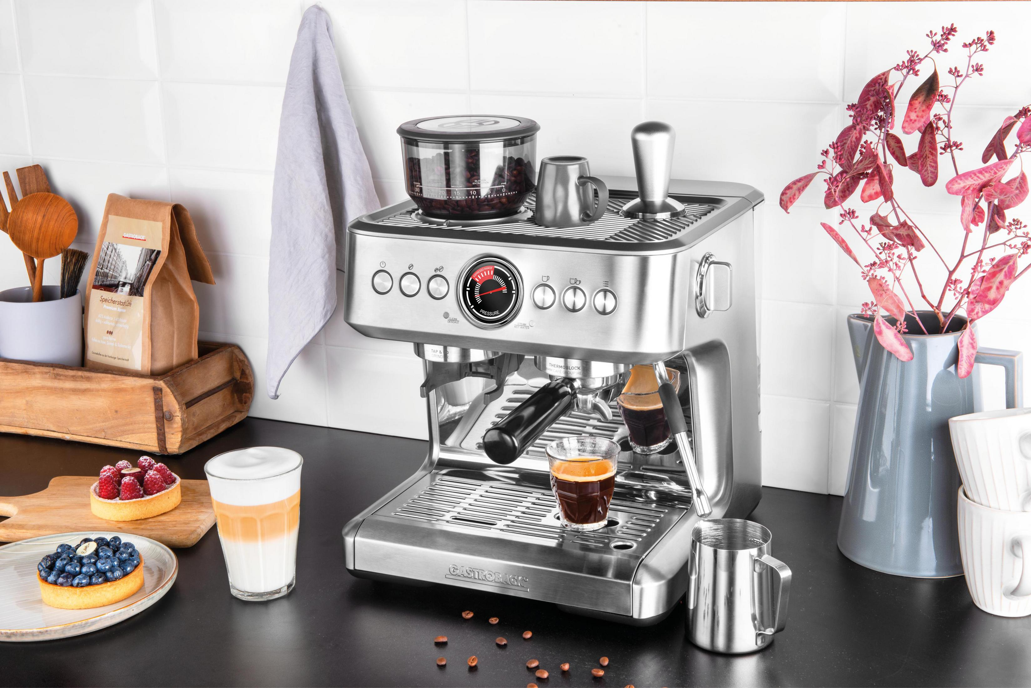 Macchina per espresso argentata con accessori. Include chicchi di caffè, una crostata e un latte.