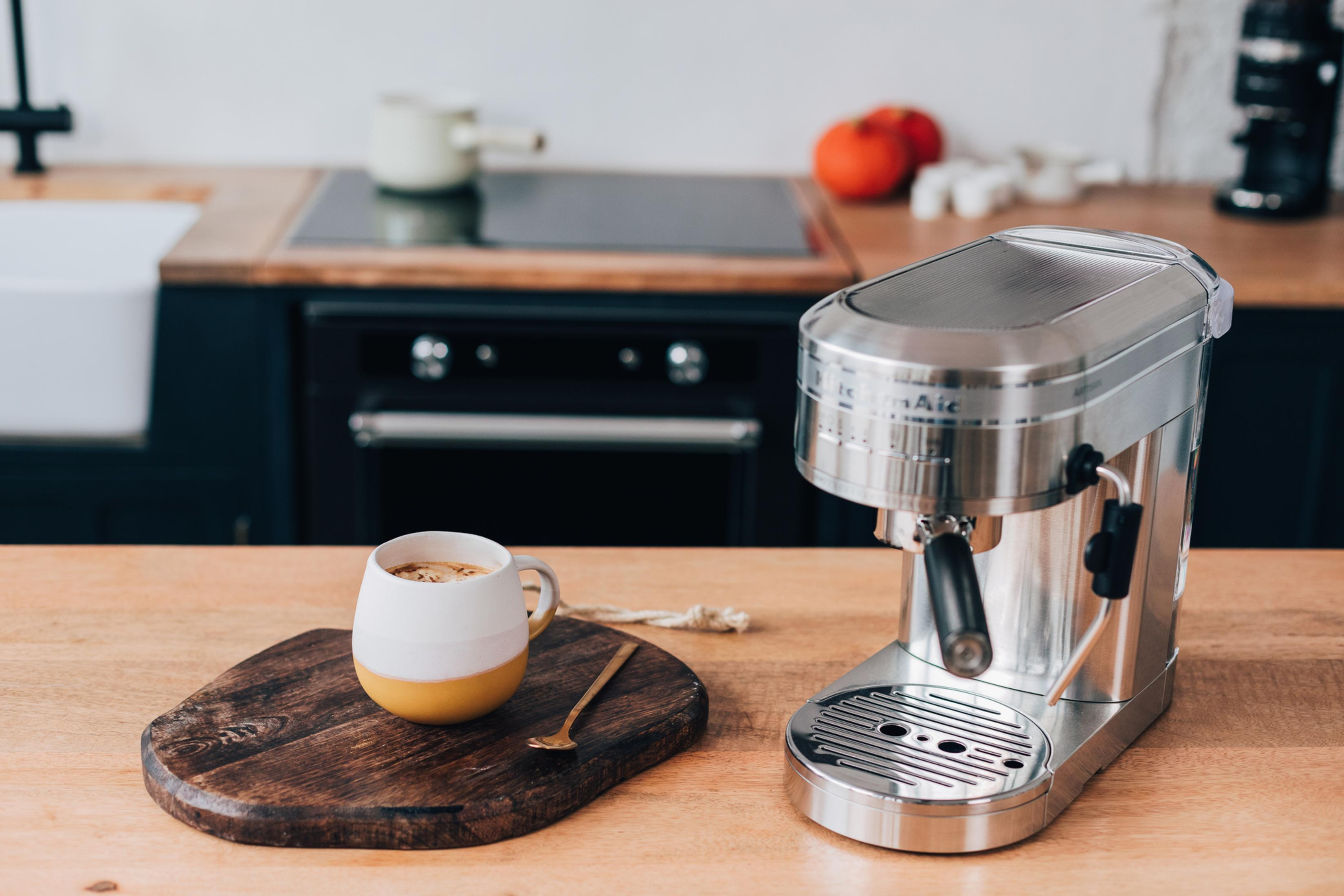Eine silberne Espressomaschine mit einer Tasse Kaffee und einem Holztablett auf einer Küchentheke.