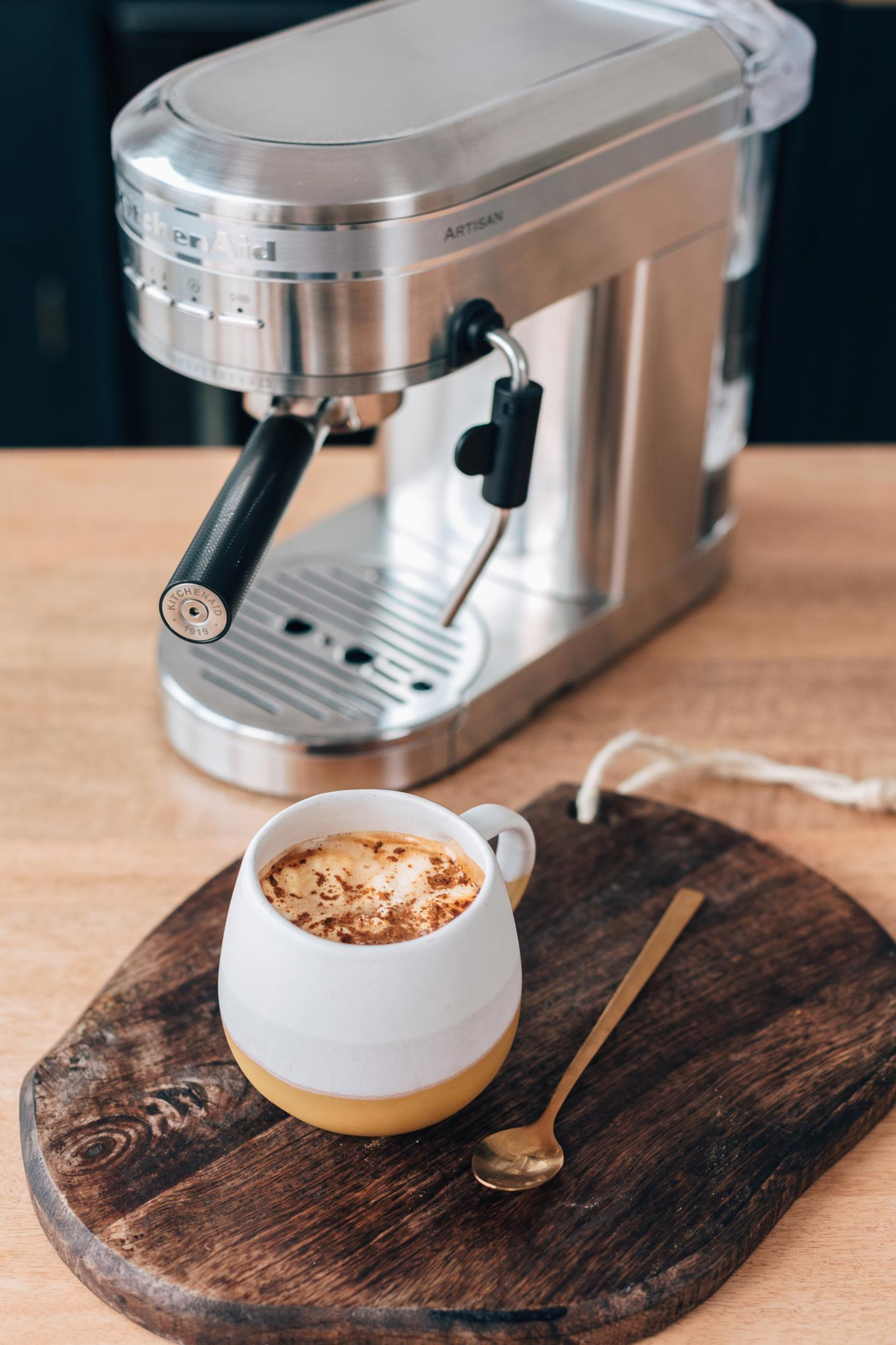 Espressomaschine mit einer Tasse Kaffee auf einem Holzbrett mit einem goldenen Löffel.