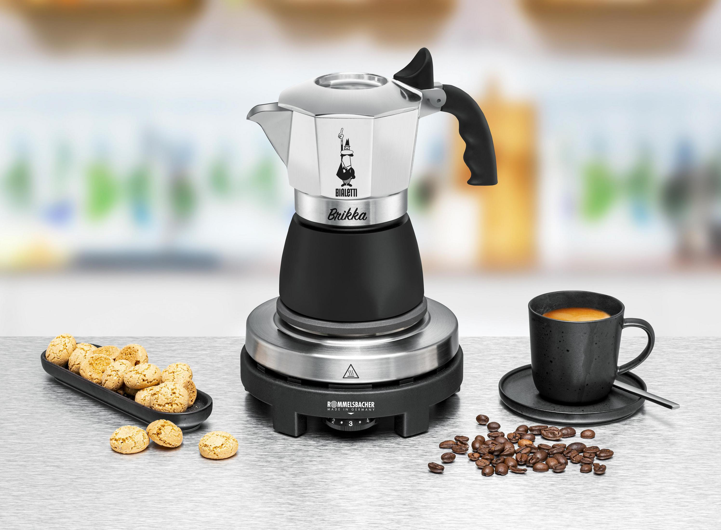 Ein silberner und schwarzer Bialetti Brikka Espressokocher mit Tasse und Keksen daneben.