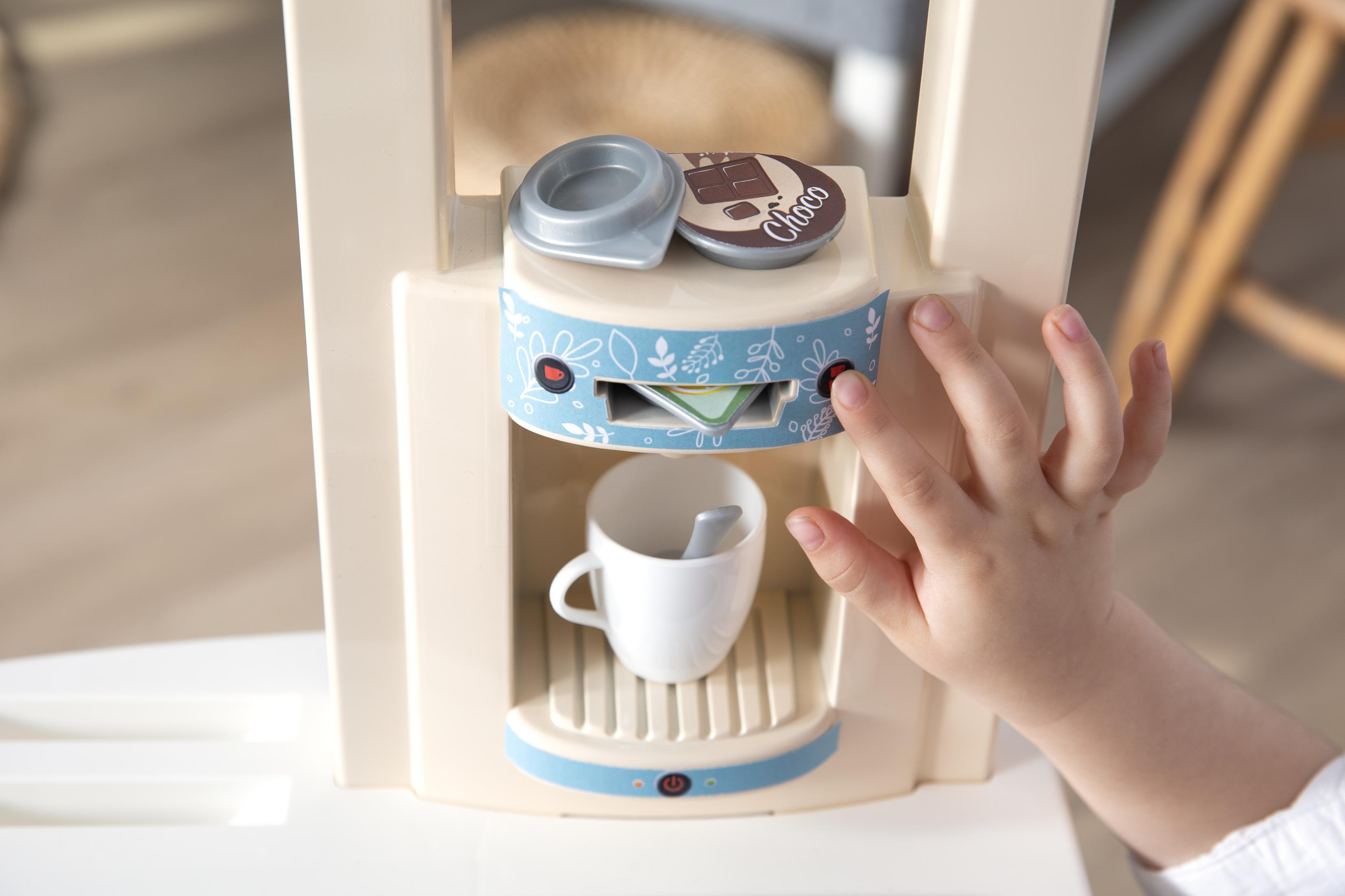 Ręka dziecka naciska przycisk na zabawkowym ekspresie do kawy z filiżanką poniżej.