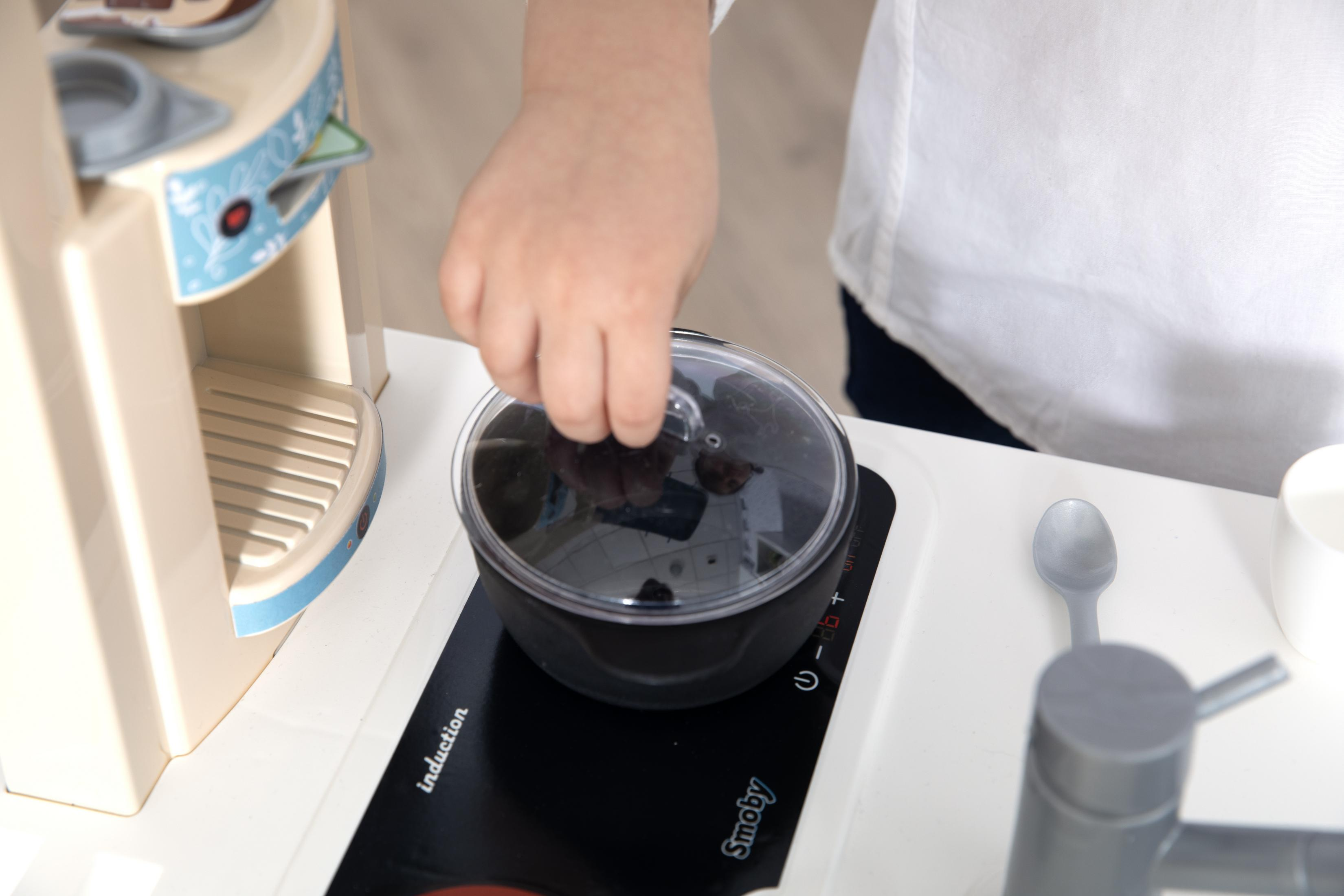 Ręka dziecka umieszcza pokrywkę na czarnym garnku na zabawkowym palniku indukcyjnym.