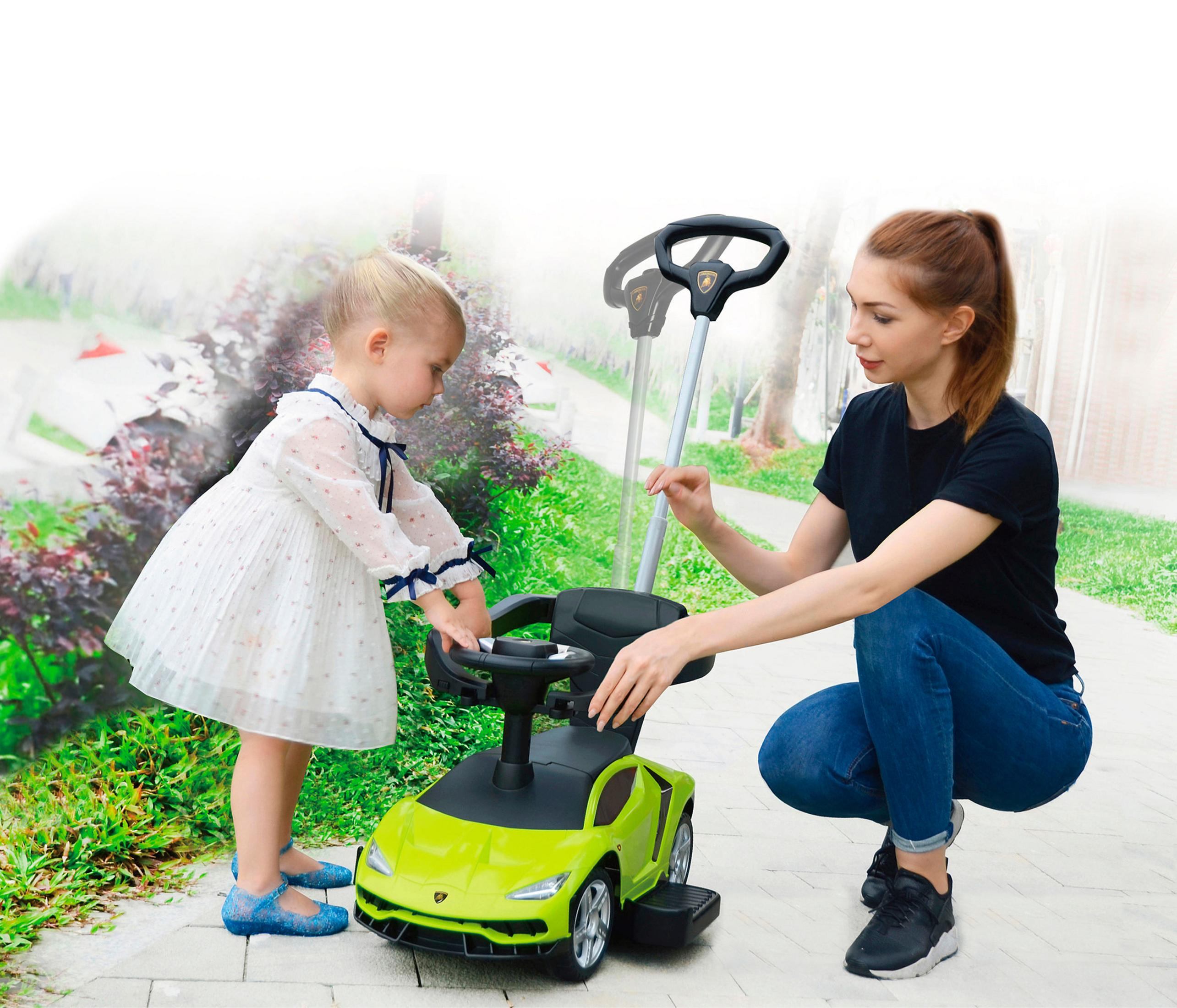 Un niño está junto a un coche de juguete verde, mientras una mujer ayuda a empujar el coche.