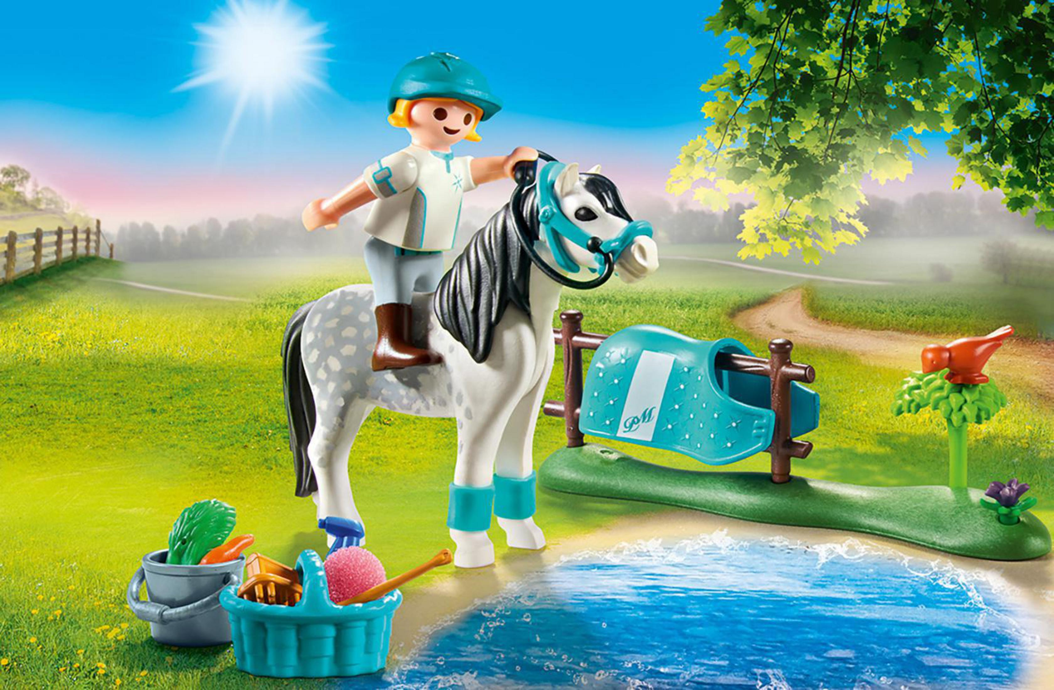 Playmobil-Figur, die auf einem Pferd auf einem Feld reitet. Es gibt einen kleinen Teich und einen Zaun.