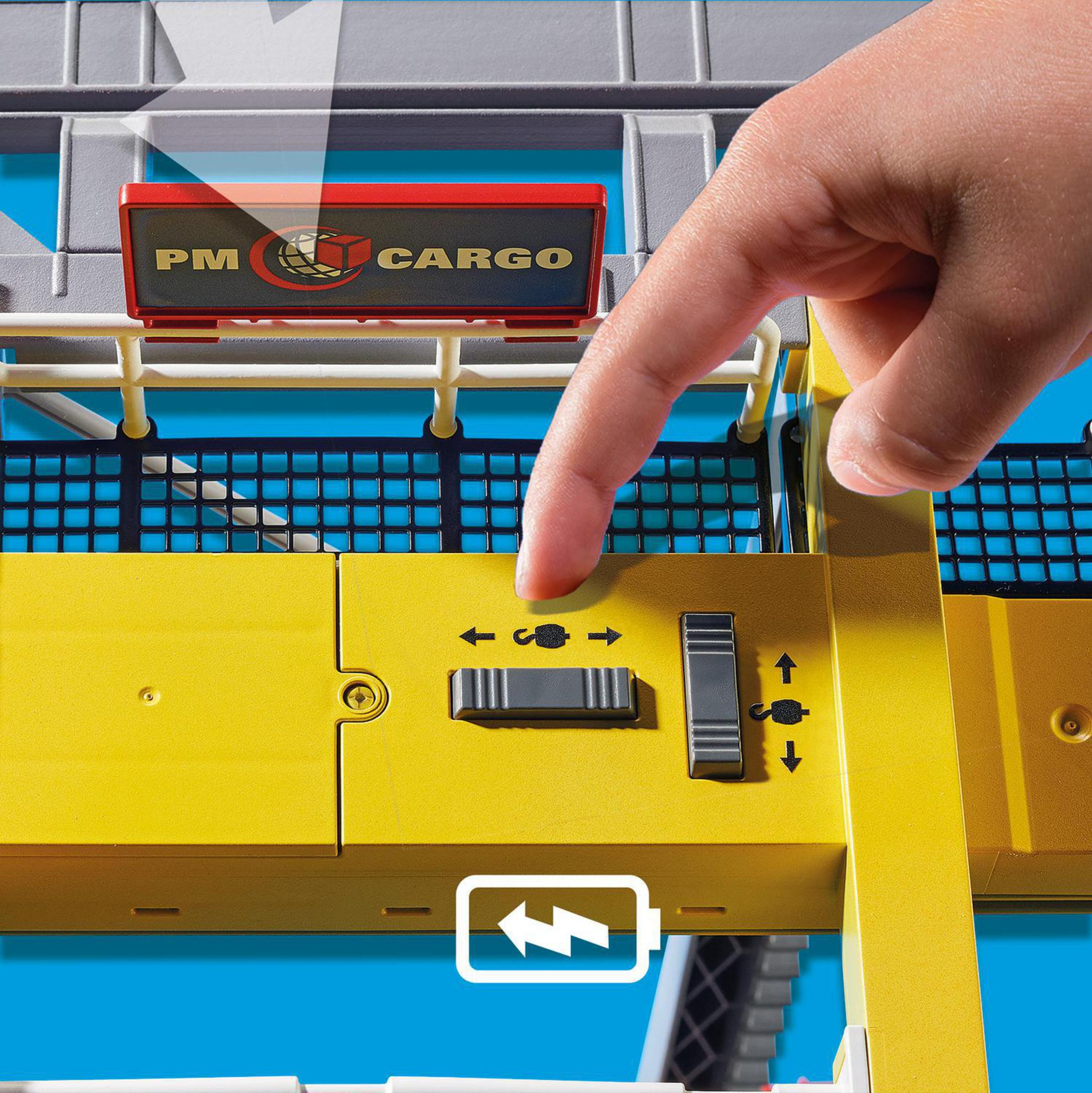 Hand drückt Knopf an Playmobil-Frachtkran, mit Batteriesymbol und Dockelementen.