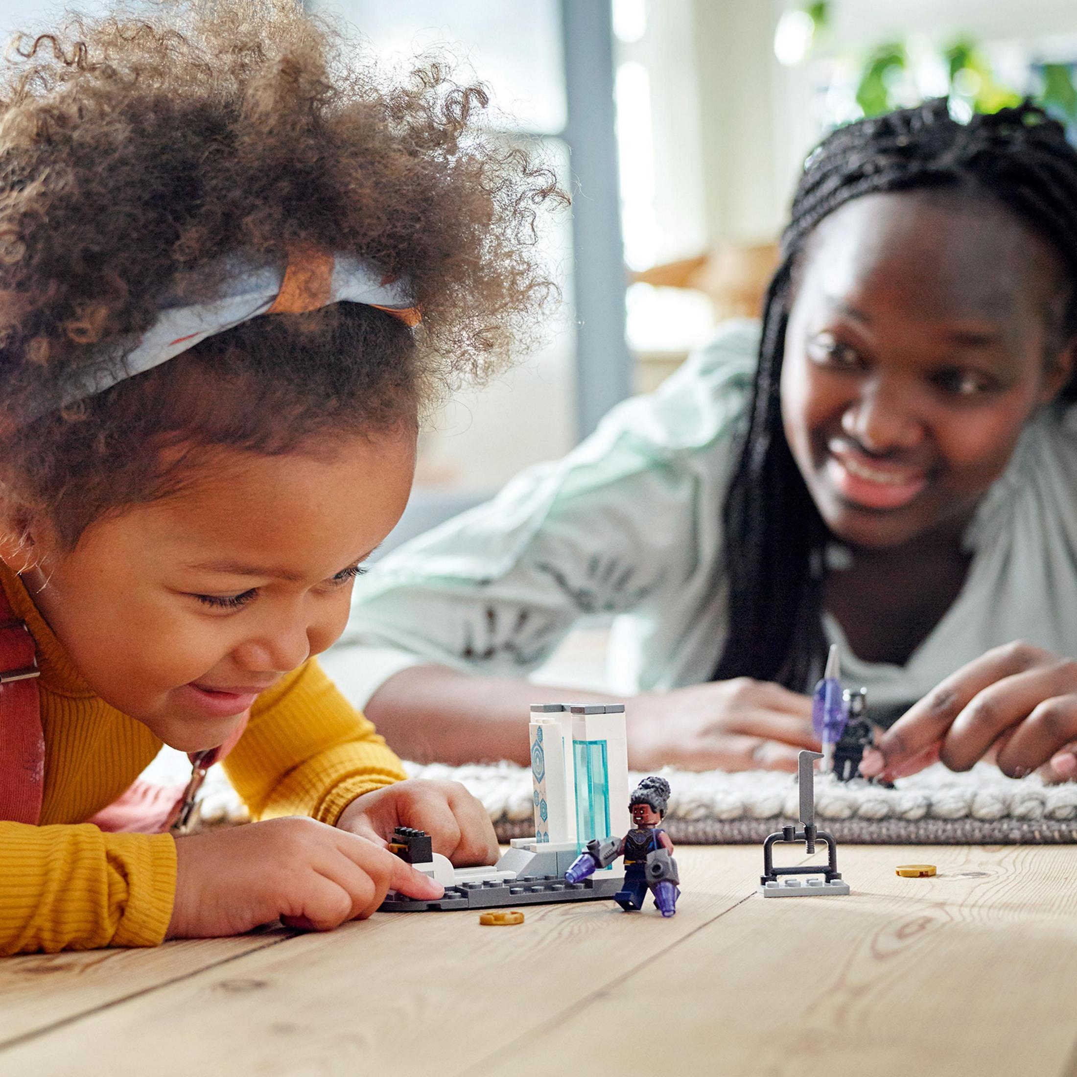 Dziecko i dorosły bawią się figurkami Lego na stole. Figurki są z Czarnej Pantery.