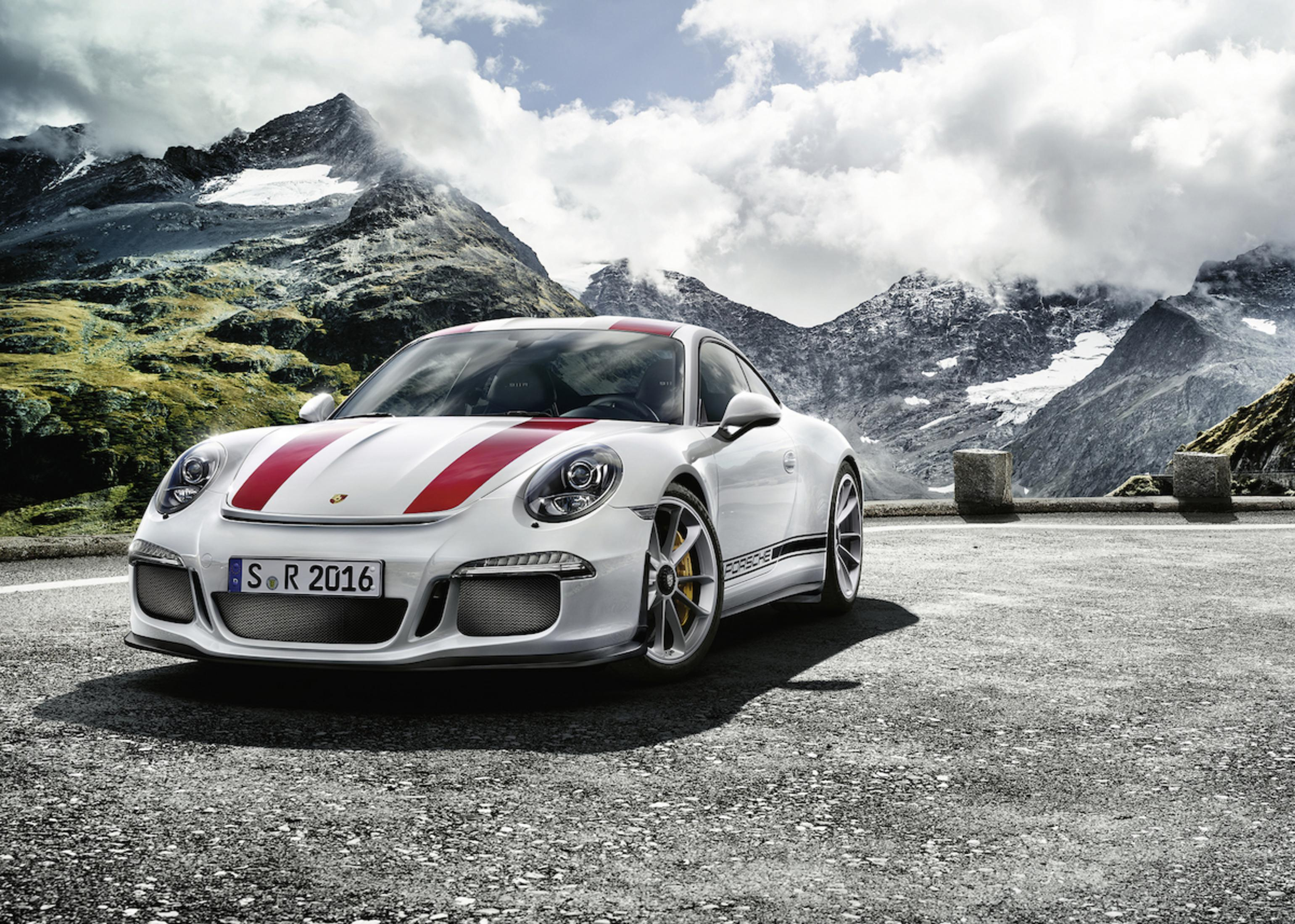 Witte Porsche sportwagen met rode strepen op bergweg, bewolkte hemel.