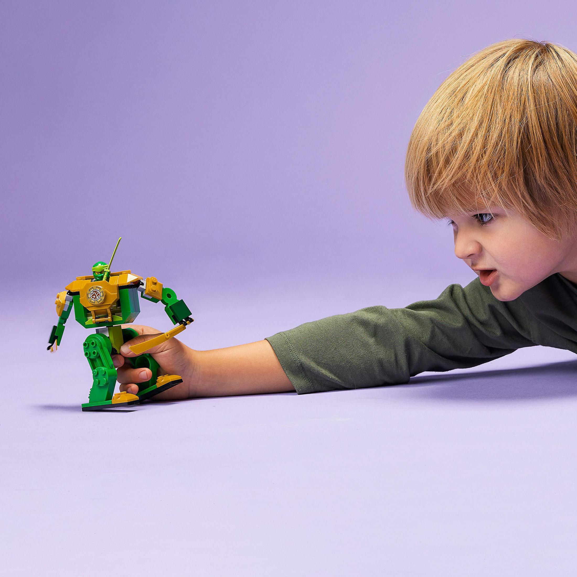 Un niño mira un juguete de robot Lego verde y amarillo sobre un fondo morado.
