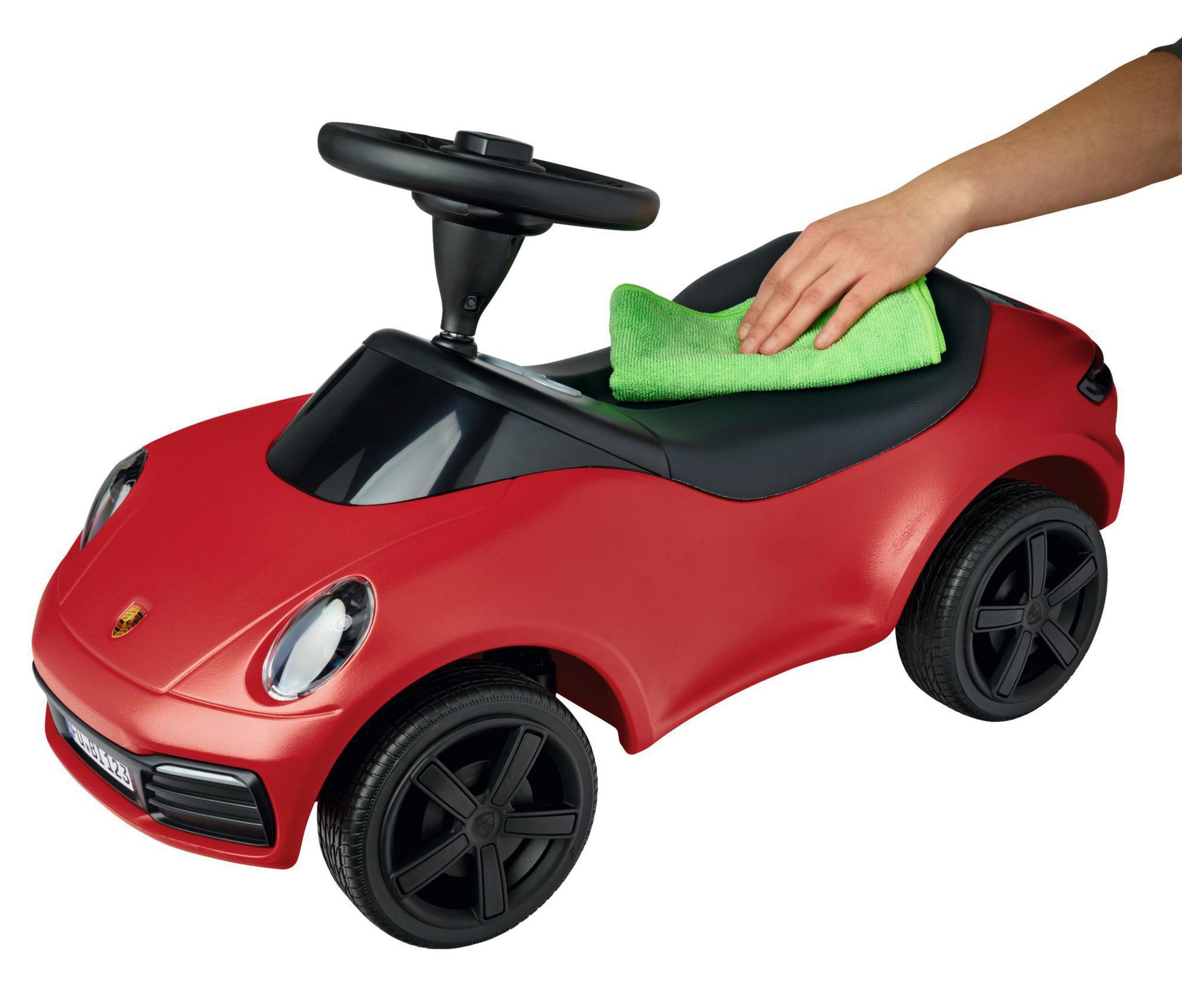 Roter Spielzeug-Porsche mit schwarzen Rädern und einem schwarzen Lenkrad, der mit einem grünen Tuch abgewischt wird.