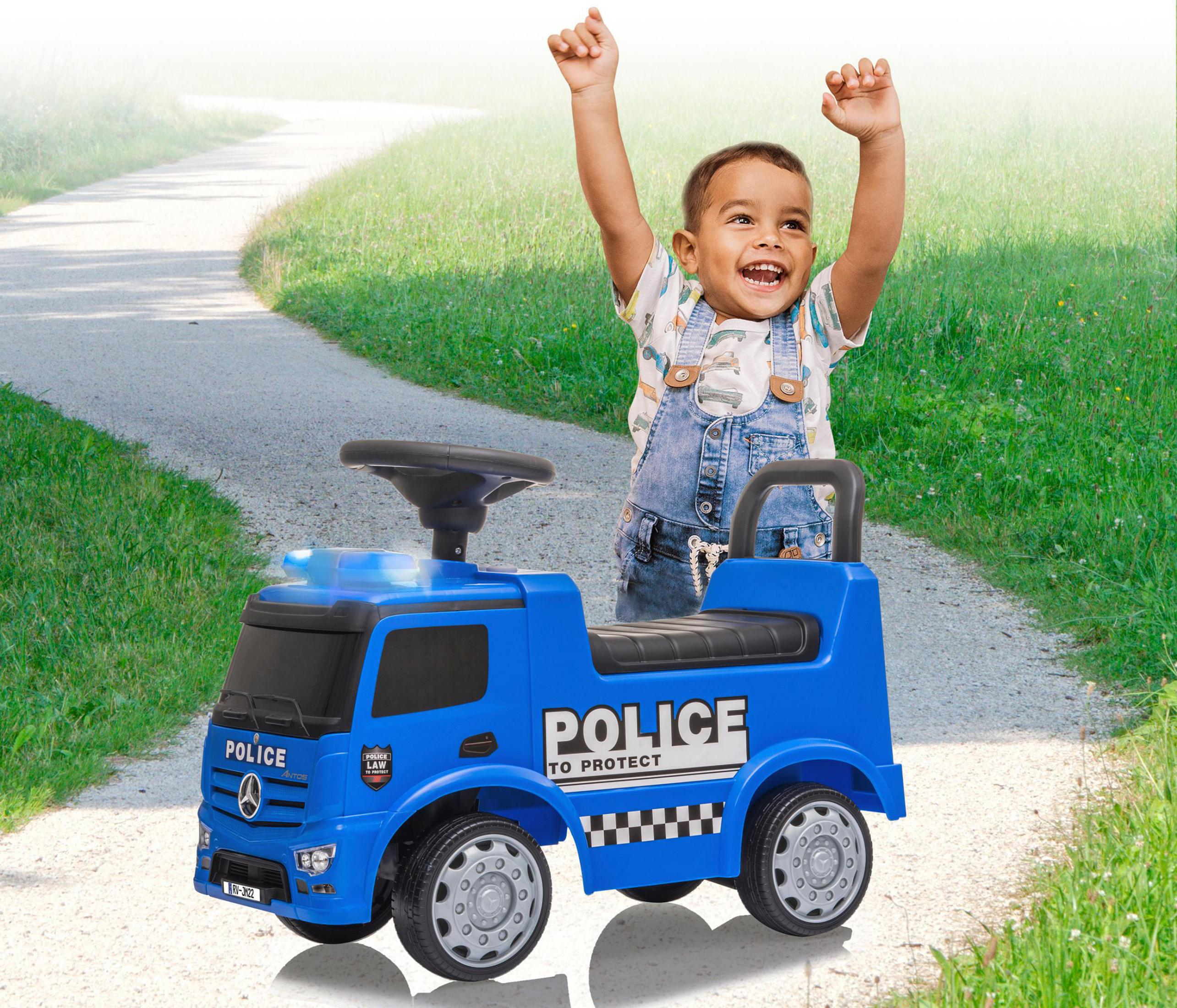 Ein Kind sitzt auf einem blauen Polizei-Spielzeug-LKW und hebt freudig die Arme auf einem Weg.