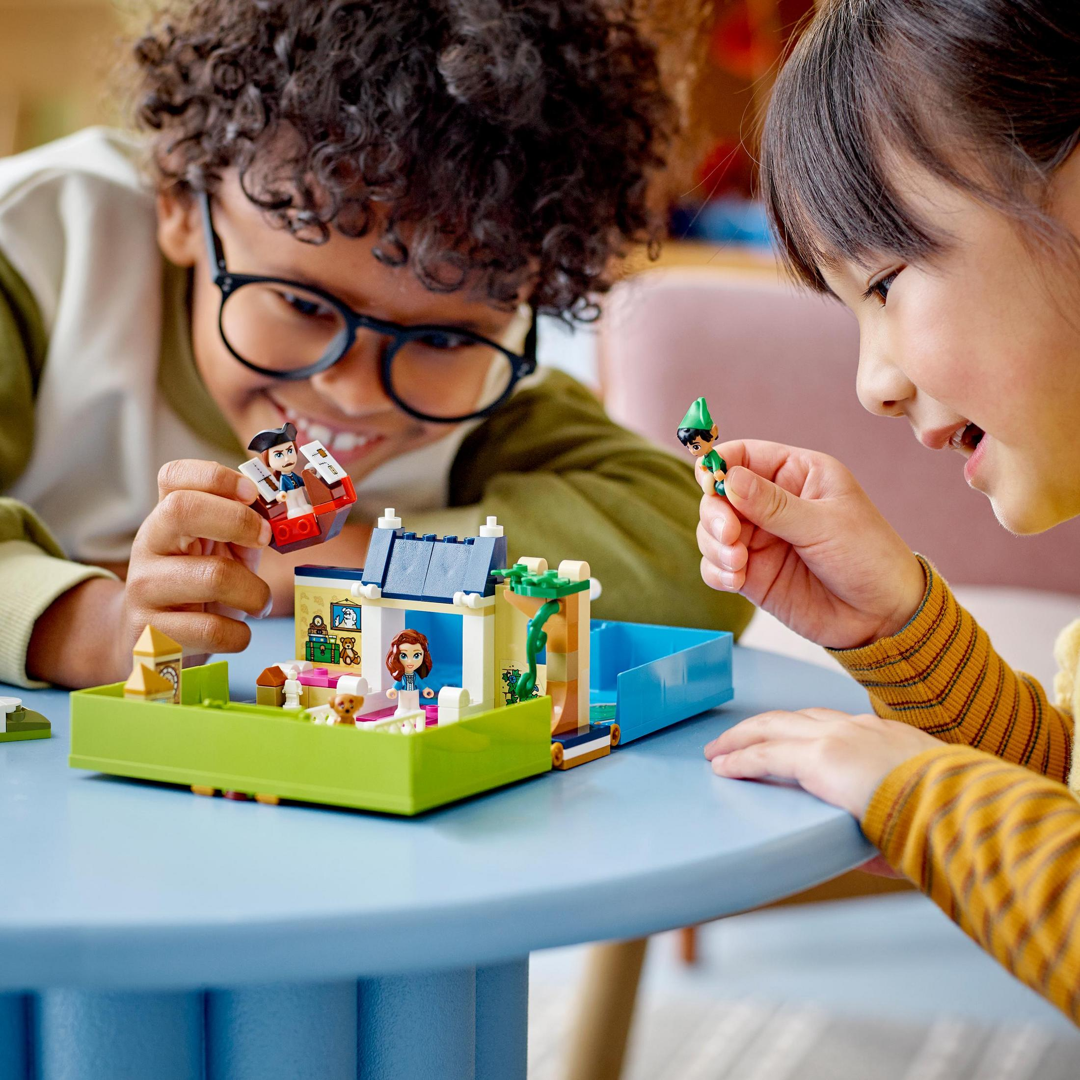 Kinderen spelen met een LEGO-huisset op een blauwe tafel.