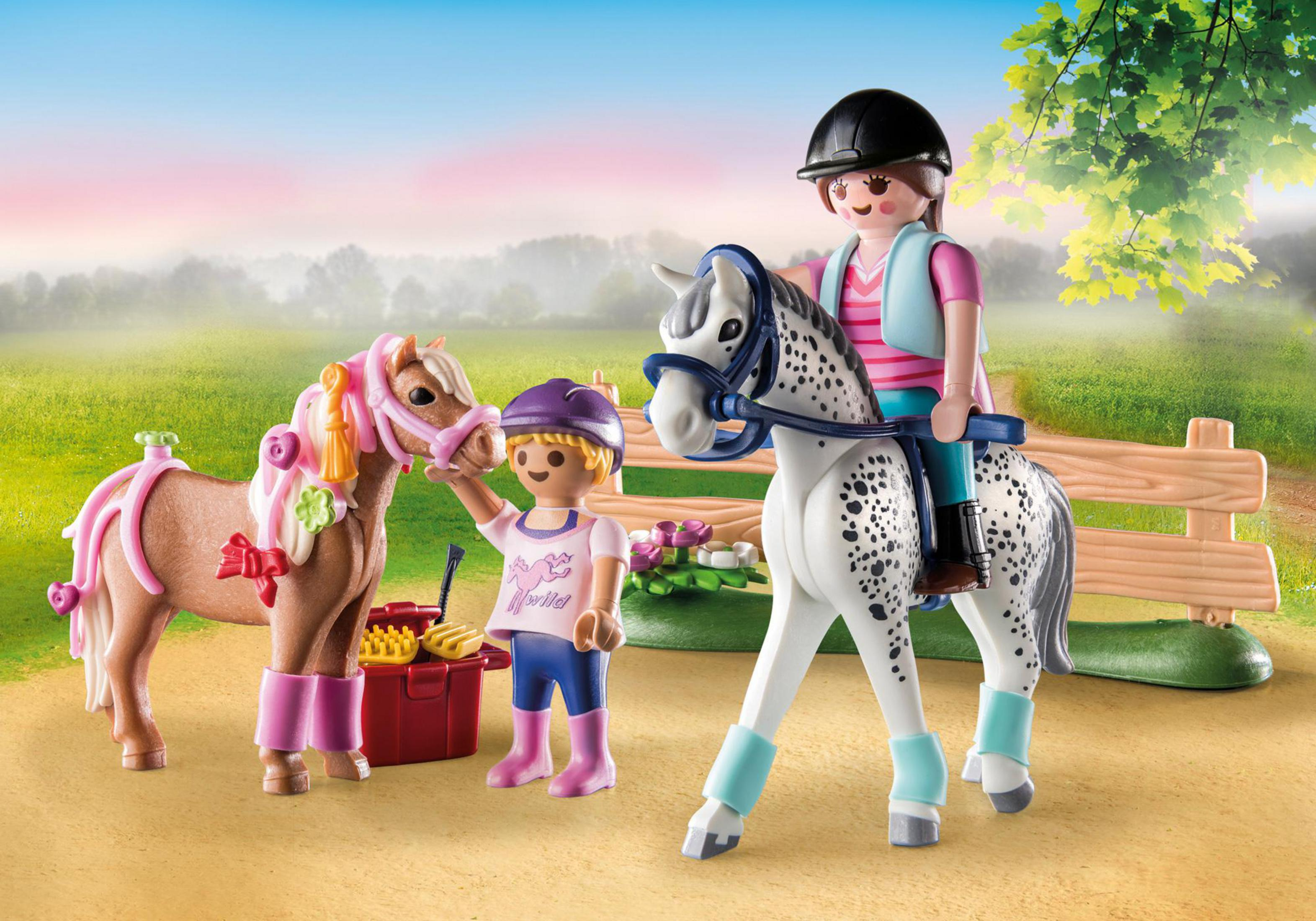 Personaggi giocattolo di cavalli e cavalieri. Un bambino striglia un pony. Un altro cavalca un cavallo maculato. Sfondo verde.