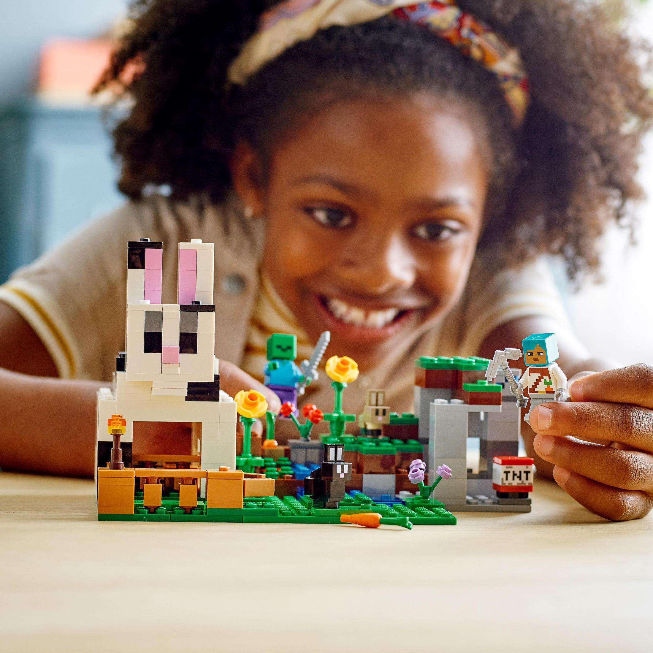 Bambina che gioca con un set Lego. Coniglio Lego, fiori e figure visibili. Faccia felice.