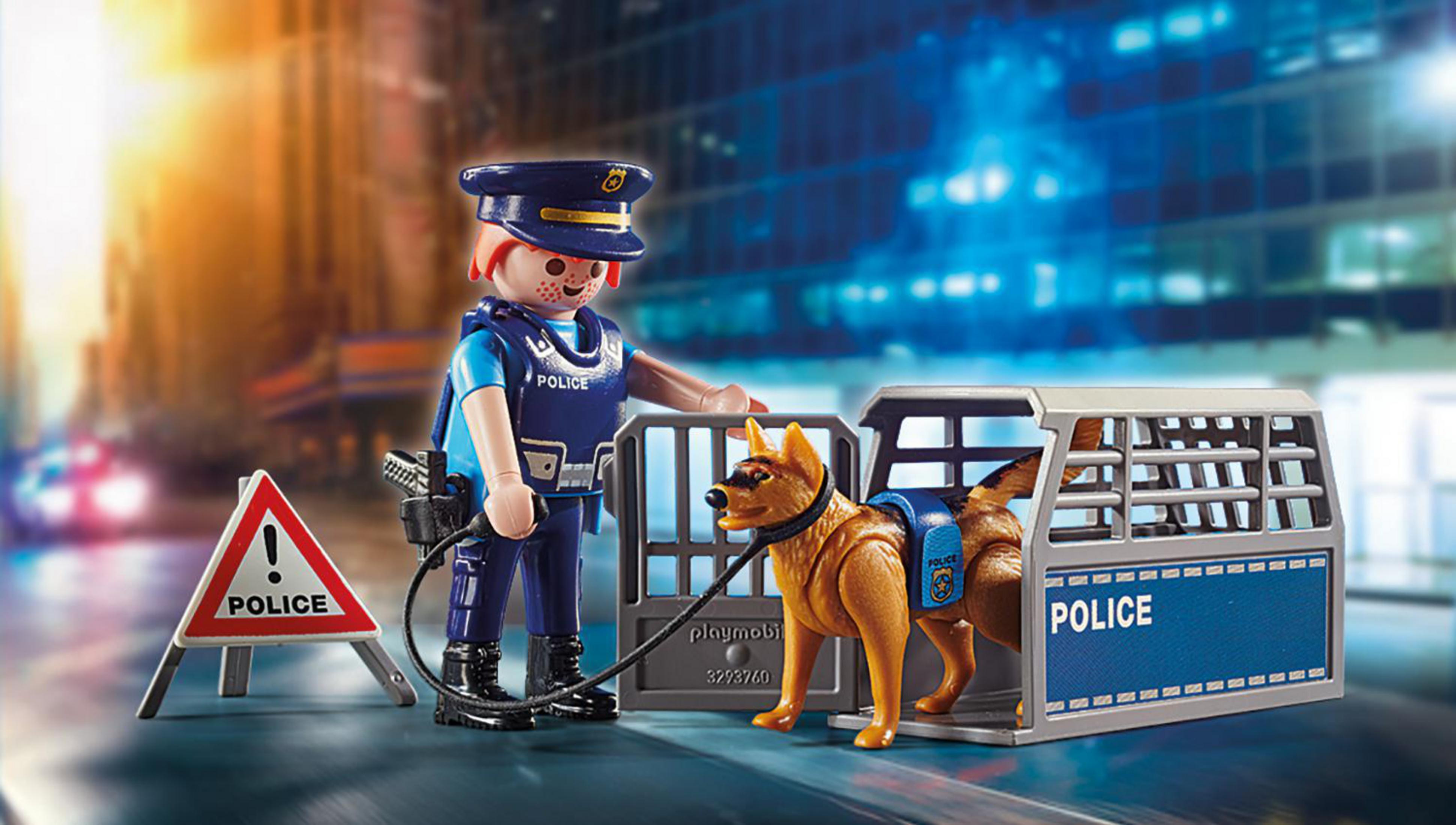 Ein Playmobil-Polizist mit Hund und Polizeiauto. Die Szene spielt auf einer Stadtstraße.