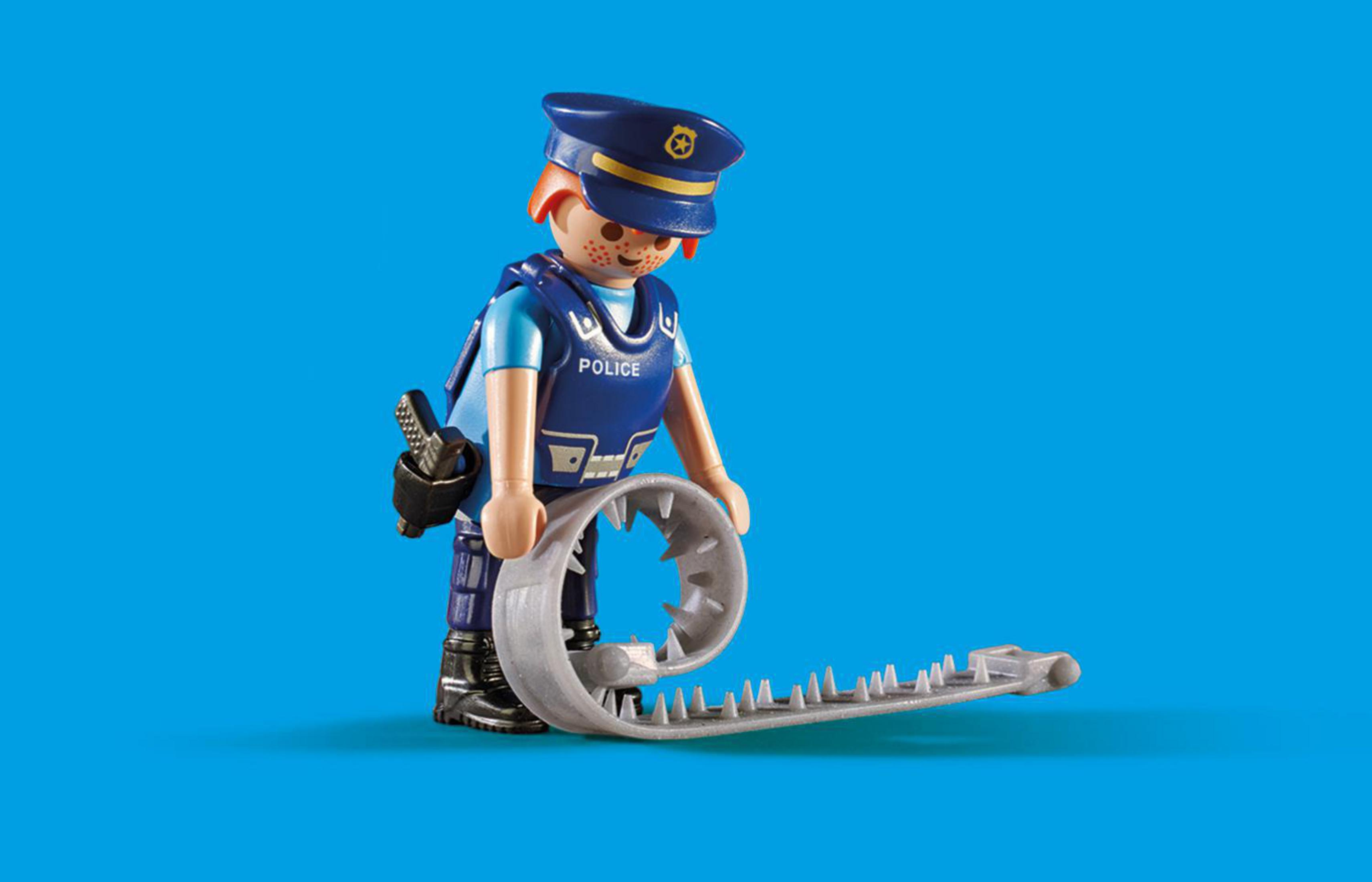 Ein Spielzeugpolizist steht mit einer Falle. Der Hintergrund ist einfarbig blau.