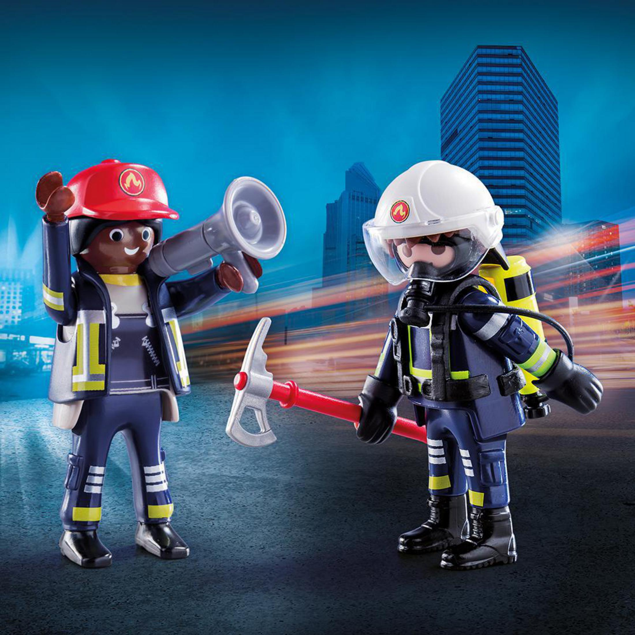 Playmobil-Feuerwehrleute mit Helmen, Megafon und Axt. Ein Stadtbild mit Wolkenkratzer ist zu sehen.