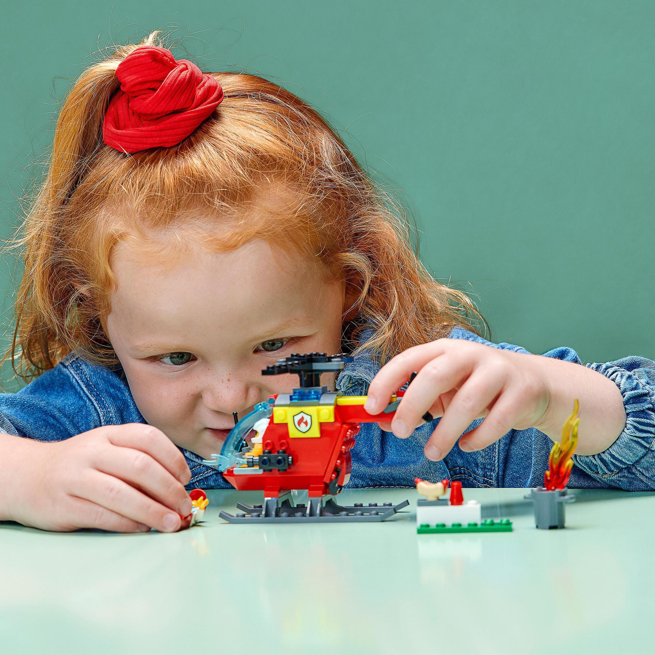 Ein junges Mädchen mit roten Haaren spielt mit einem roten Lego-Hubschrauber.