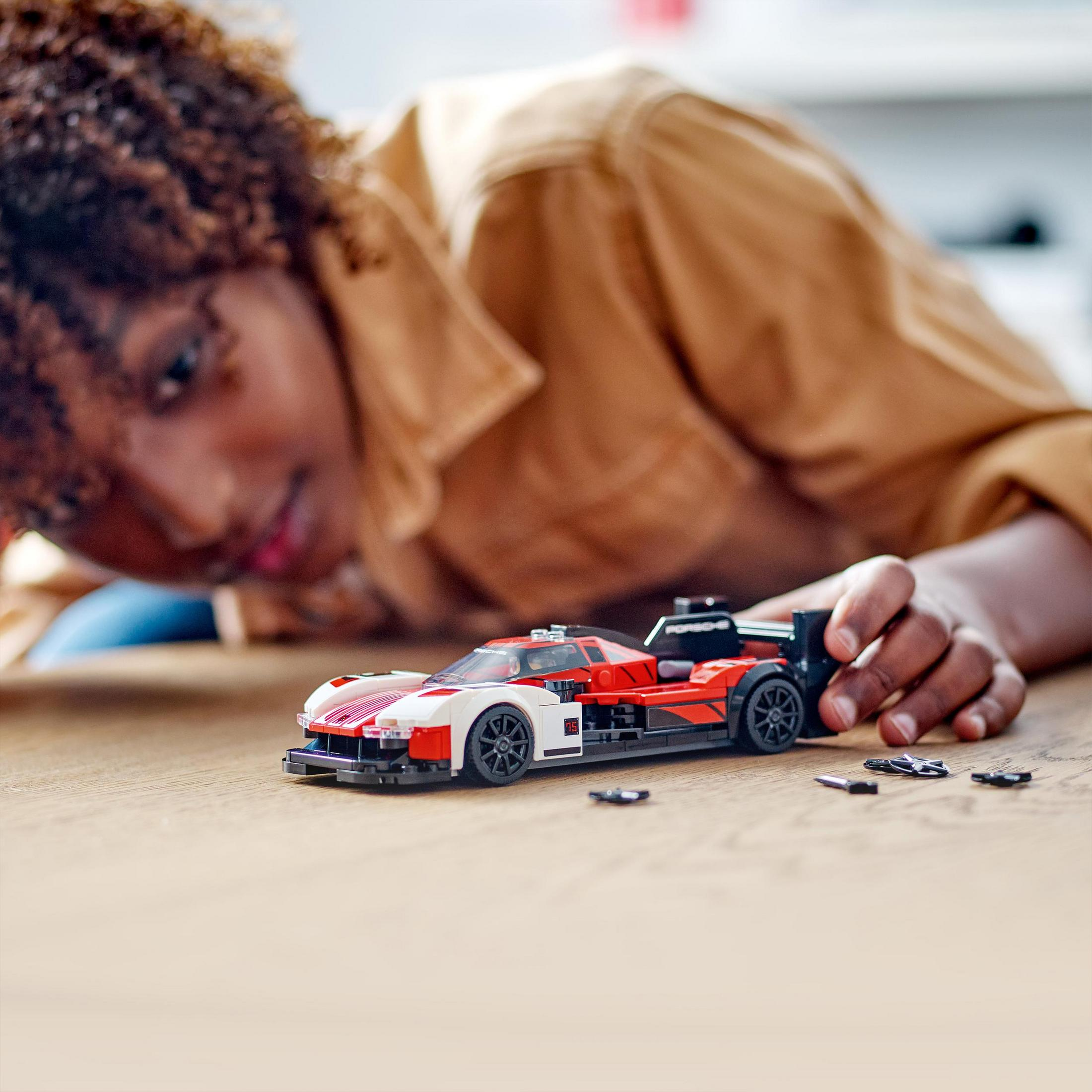 Eine Person spielt mit einem rot-weißen Spielzeug-Porsche auf einem Holztisch.