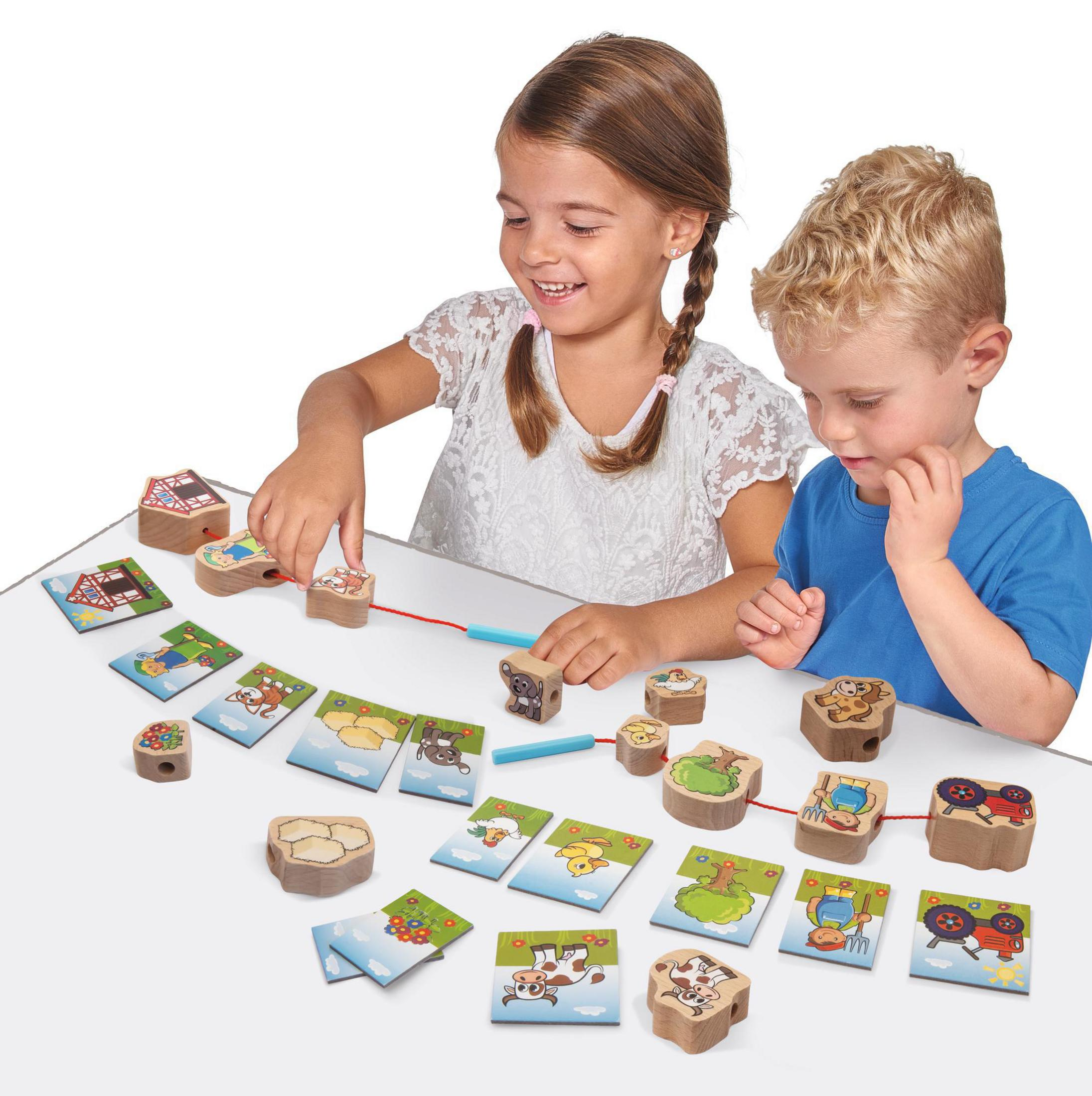 Zwei Kinder spielen mit Holzblöcken und Karten auf einem weißen Tisch. Ein Wegbauspiel.
