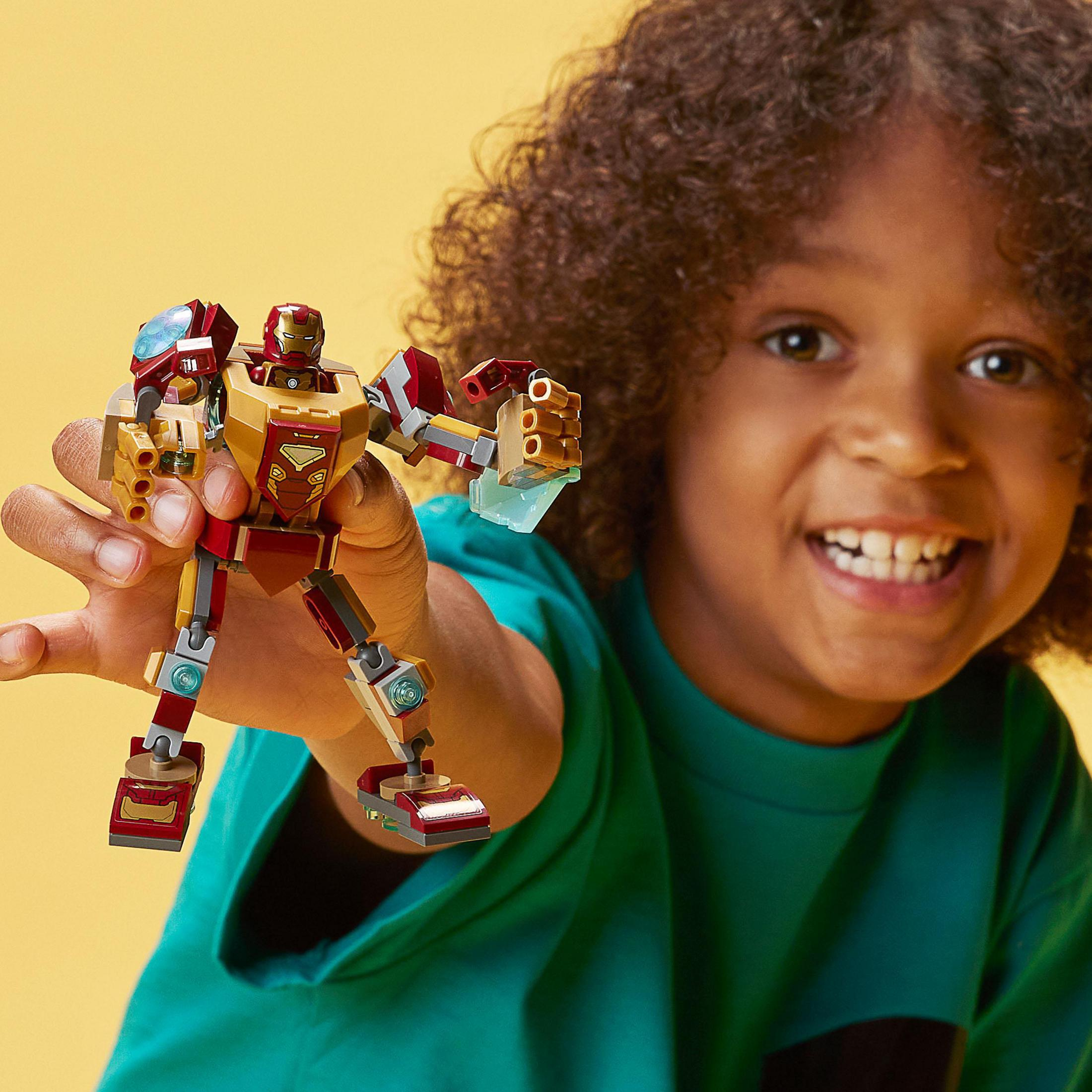 Un bambino tiene in mano un personaggio Lego Iron Man. Sfondo giallo.