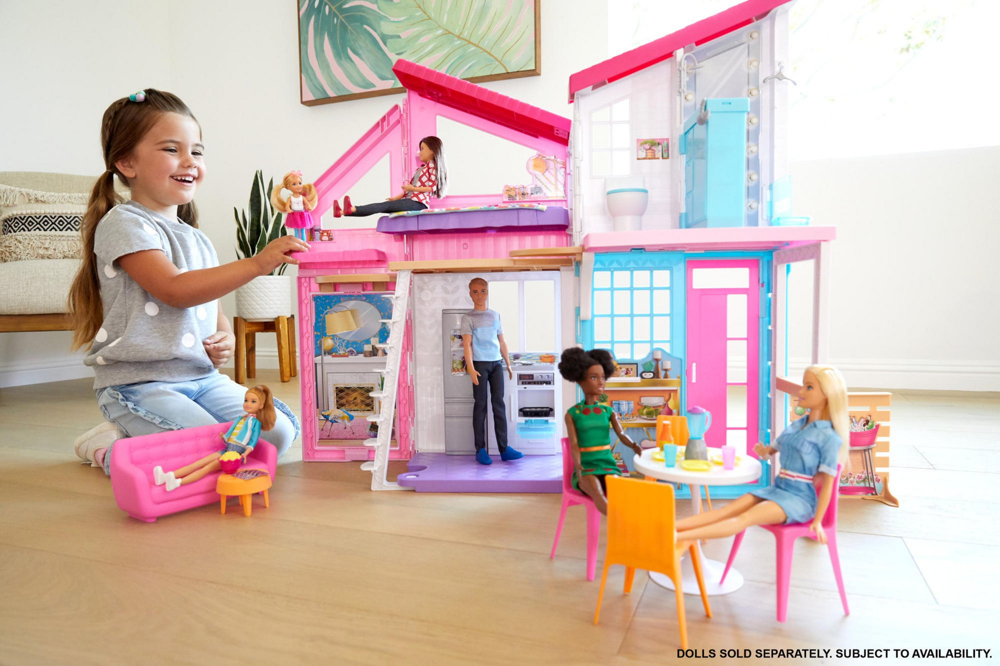 Barbie-Puppenhaus mit einem Mädchen, das mit Puppen spielt. Das Haus ist rosa und weiß.