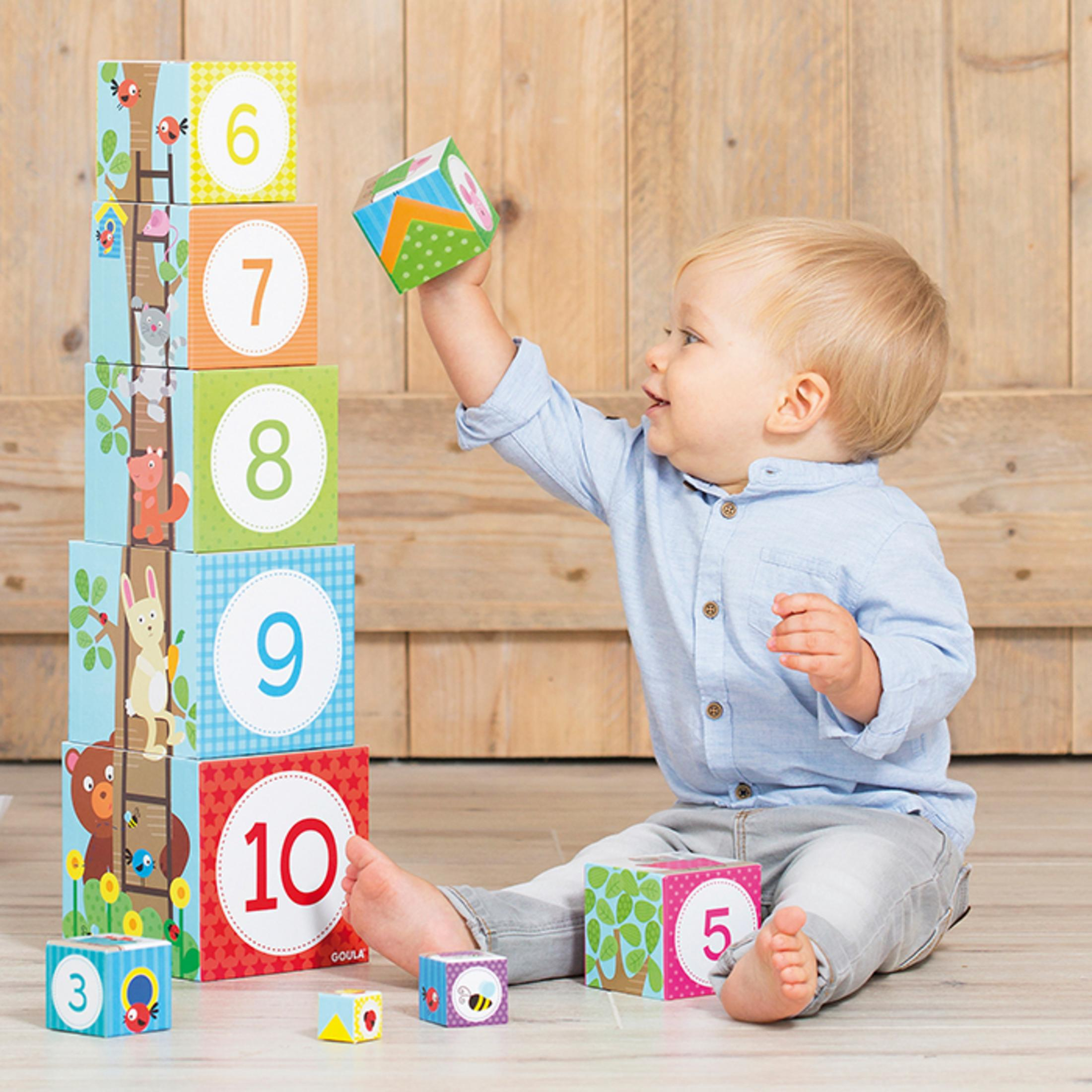 Małe dziecko bawiące się ponumerowanymi klockami ułożonymi w wieżę, siedząc na dywanie.