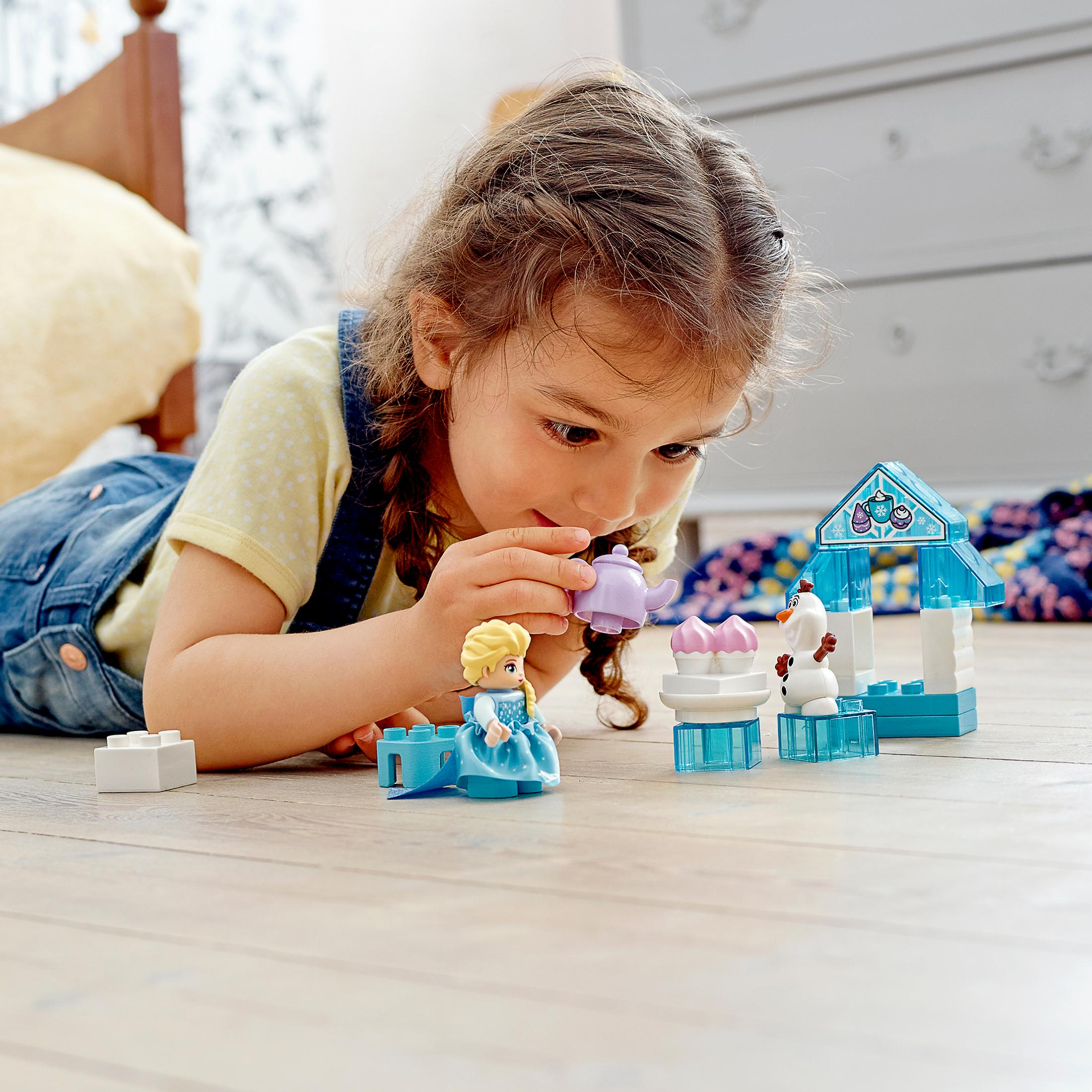 Ein junges Mädchen spielt mit Lego-Figuren von Elsa und Olaf neben einem Lego-Schloss.