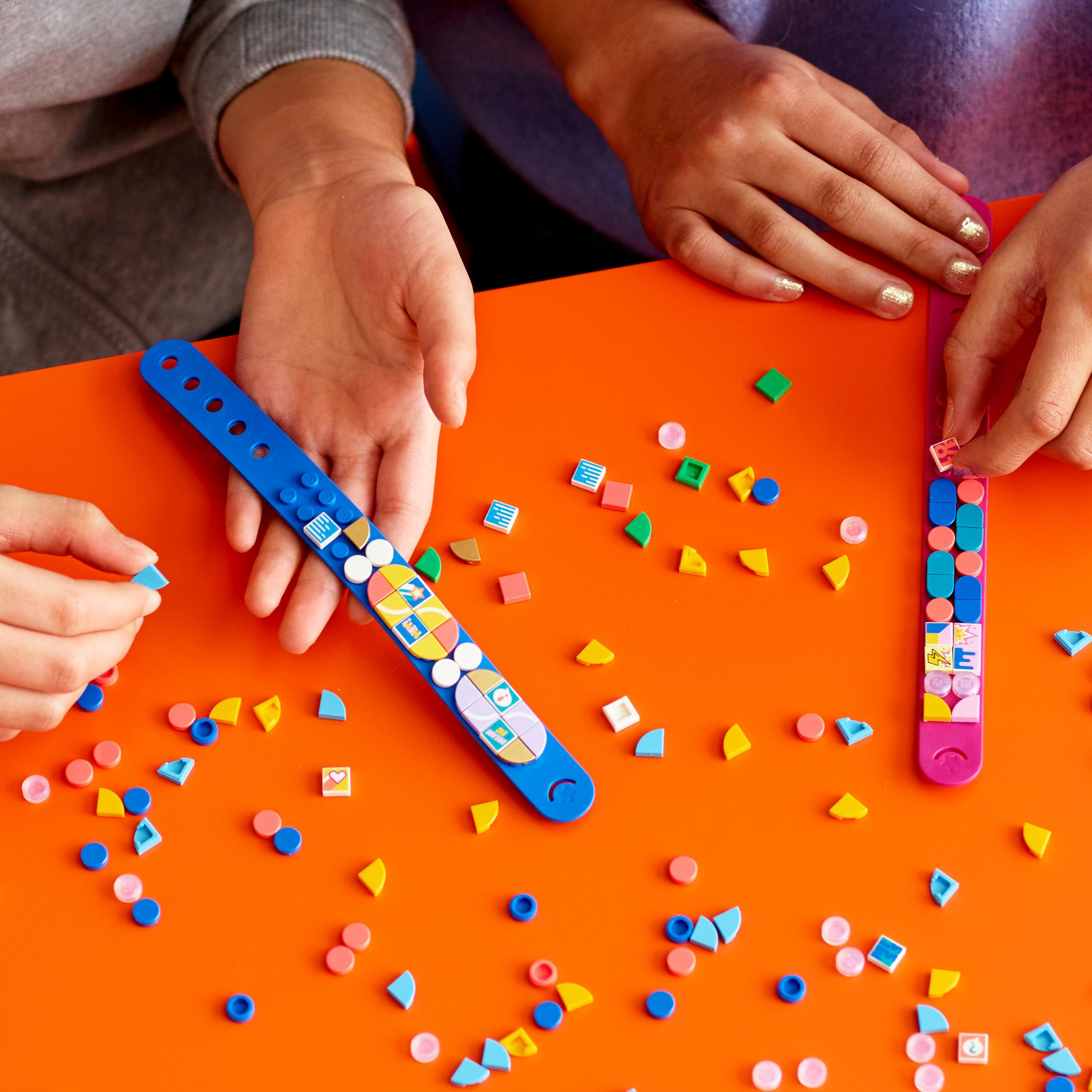 Zwei Personen dekorieren Armbänder mit bunten Lego-Teilen auf orangefarbener Fläche.
