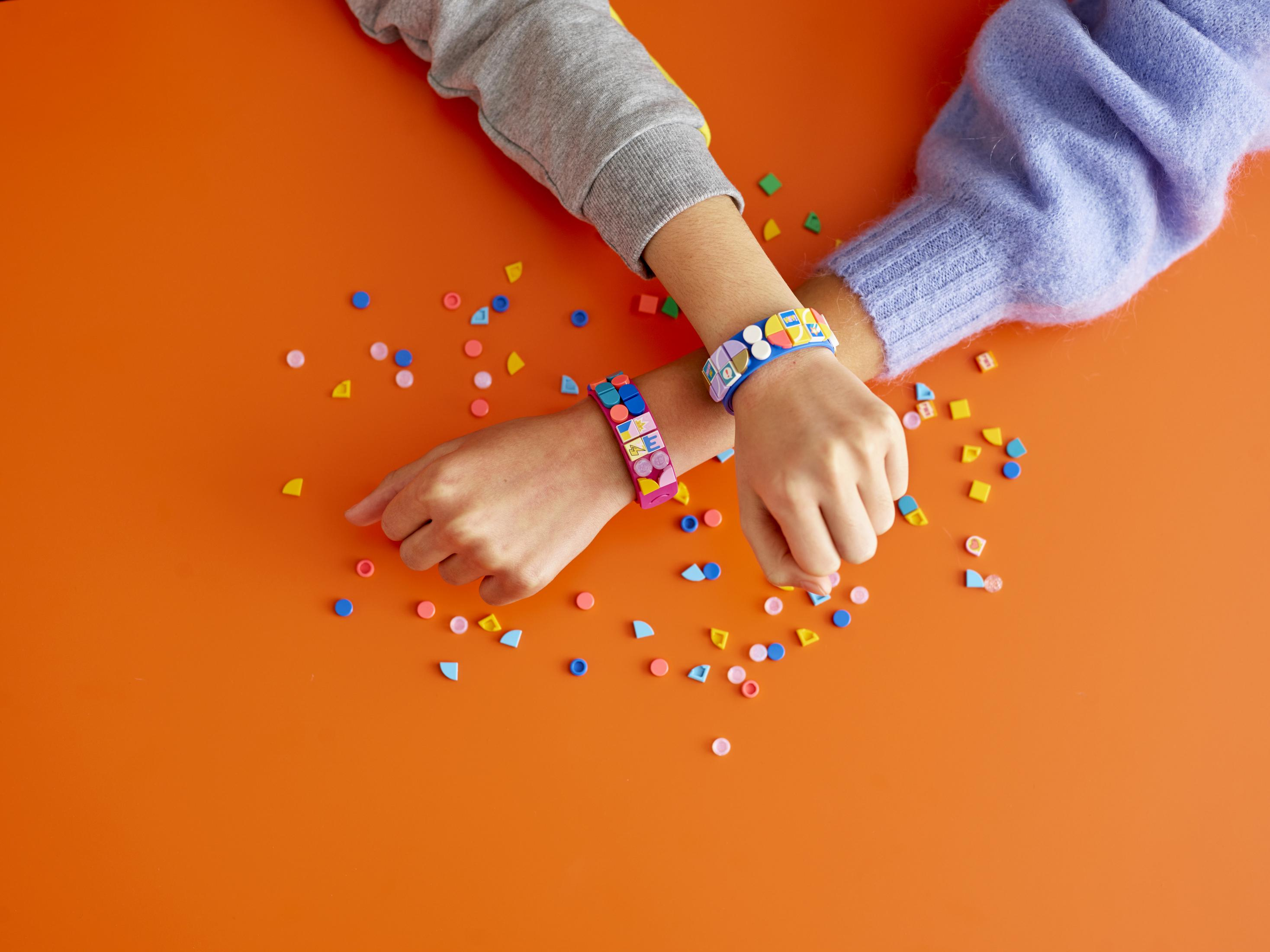 Hände mit Lego-Armbändern auf einer orangefarbenen Oberfläche, mit verstreuten Legosteinen.