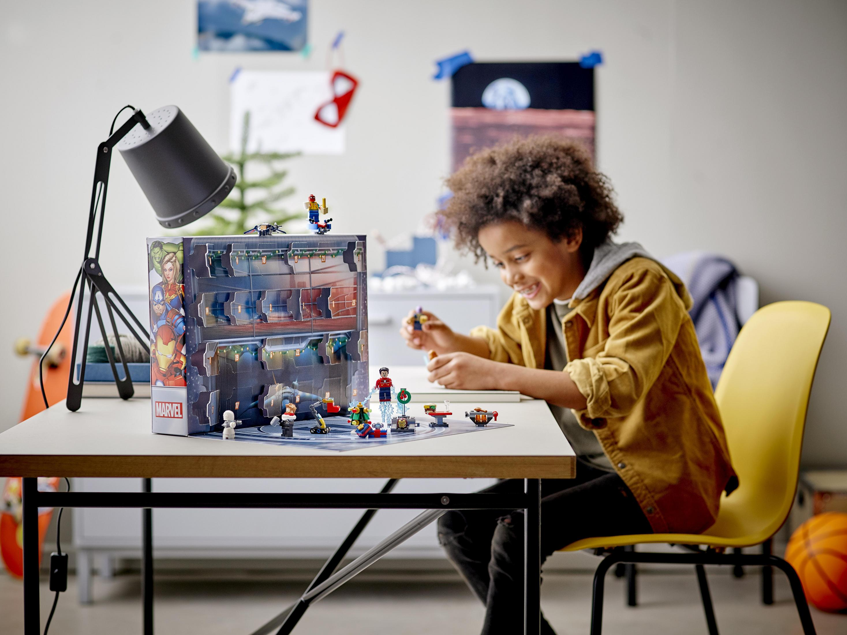 Chłopiec bawi się kalendarzem adwentowym Marvel, w pobliżu stołu i lampy.