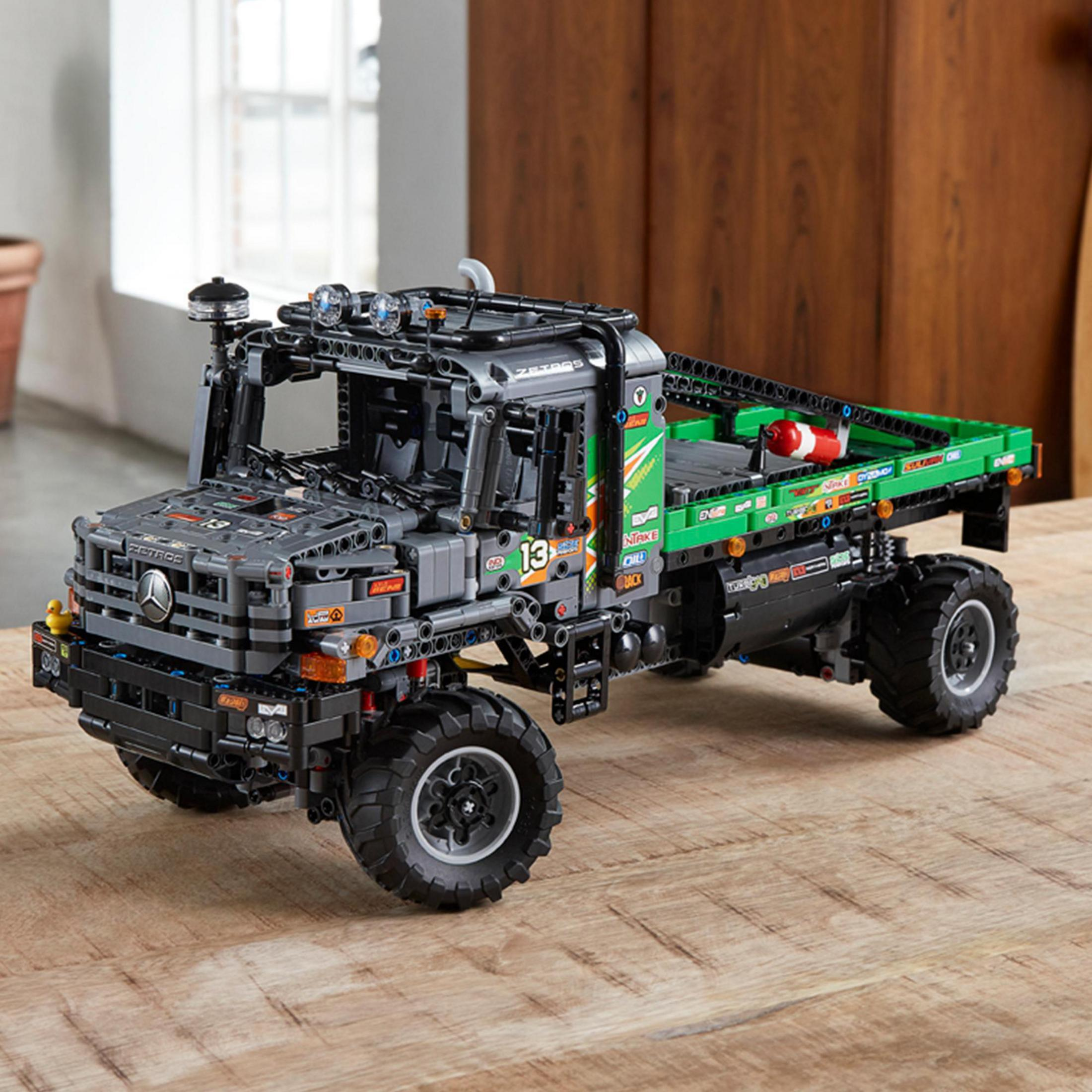 Ciężarówka Lego Technic Unimog na drewnianej powierzchni. Ciemnoszara i zielona, z dużymi kołami.