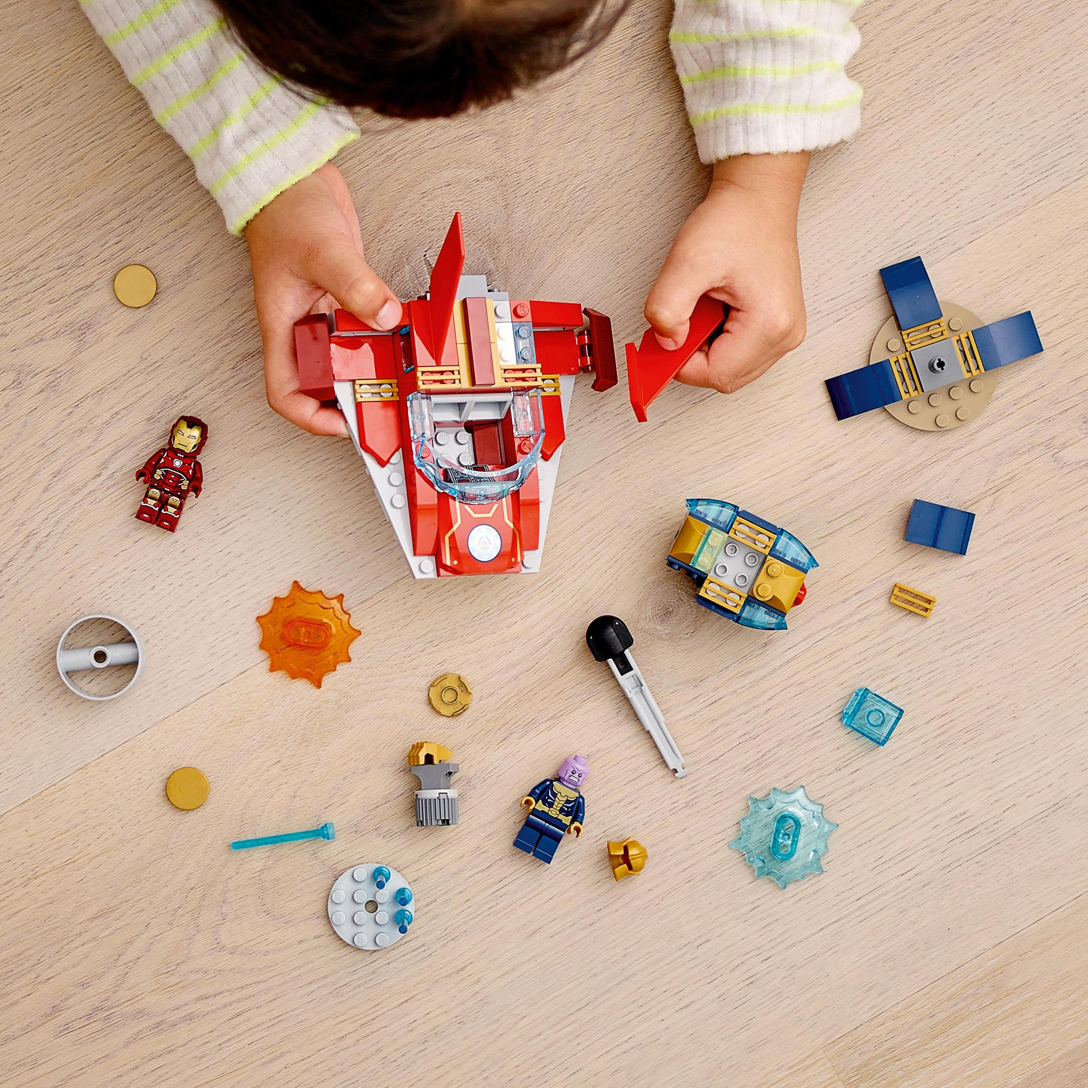 Kinderhände, die Lego-Teile zusammensetzen, darunter eine Iron Man-Figur und Raumschiffelemente, auf Holz.