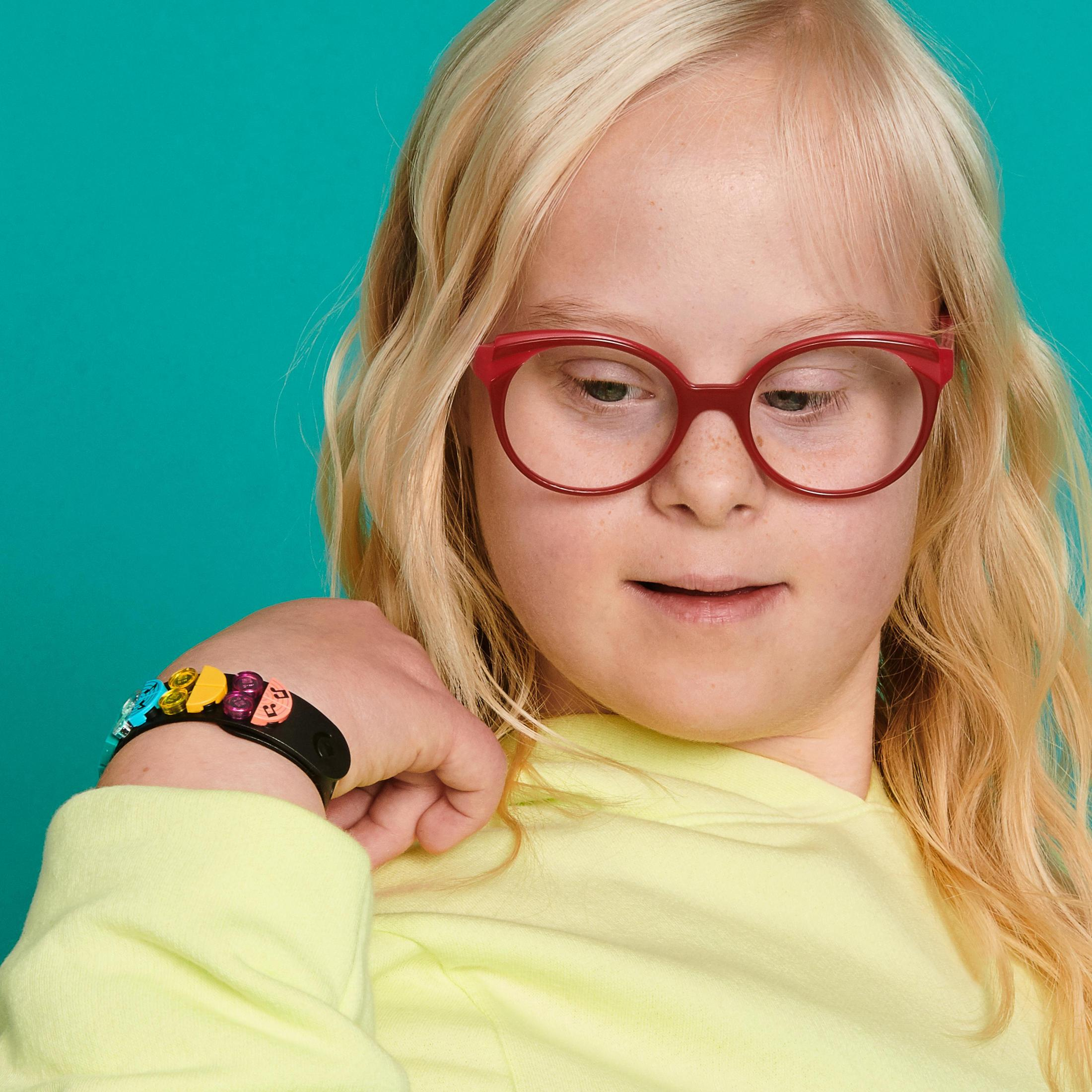 Blondynka w czerwonych okularach i kolorowej bransoletce.