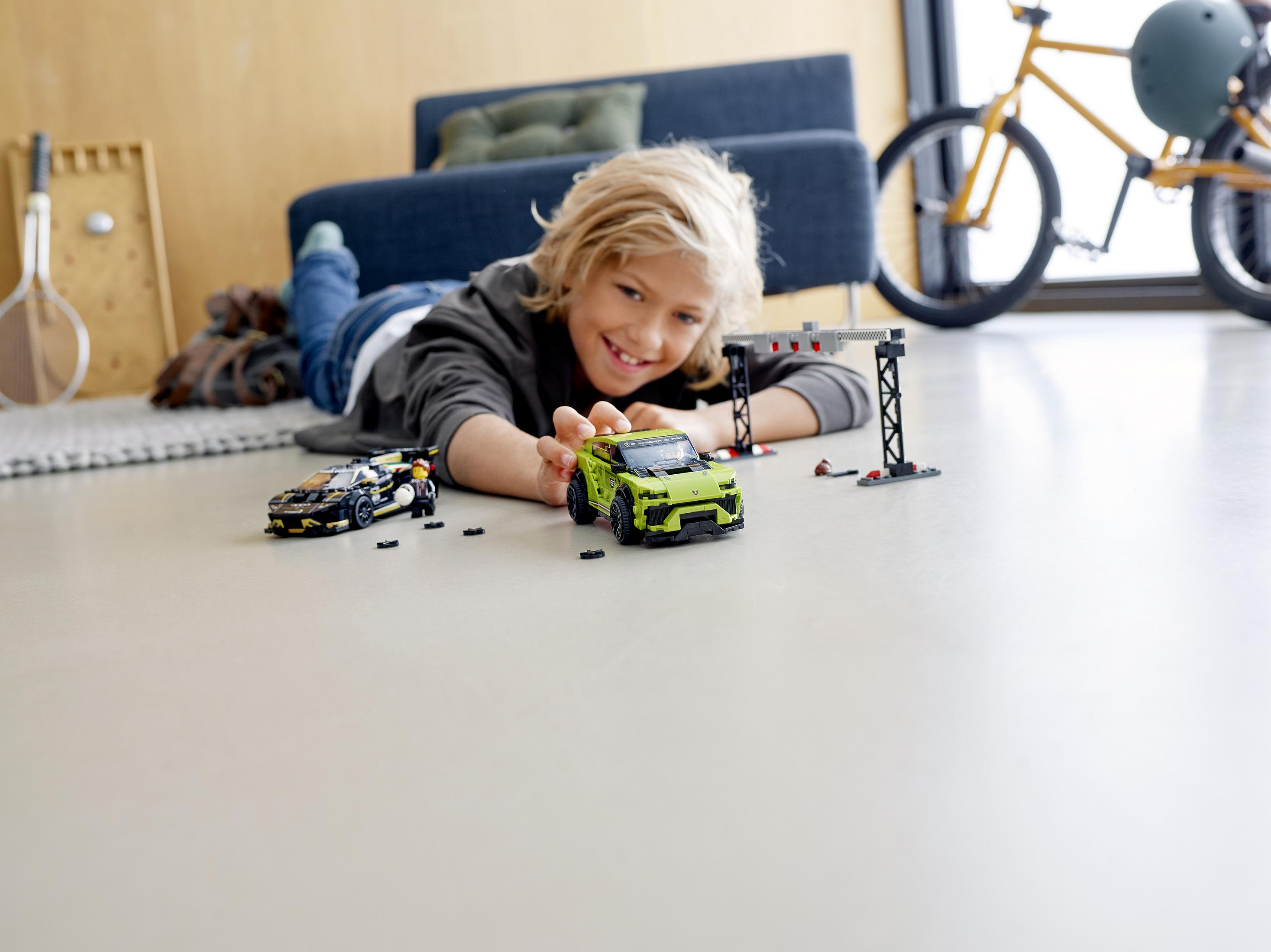 A boy lying on the floor with two toy cars, a green one and a black one, and a finish line.